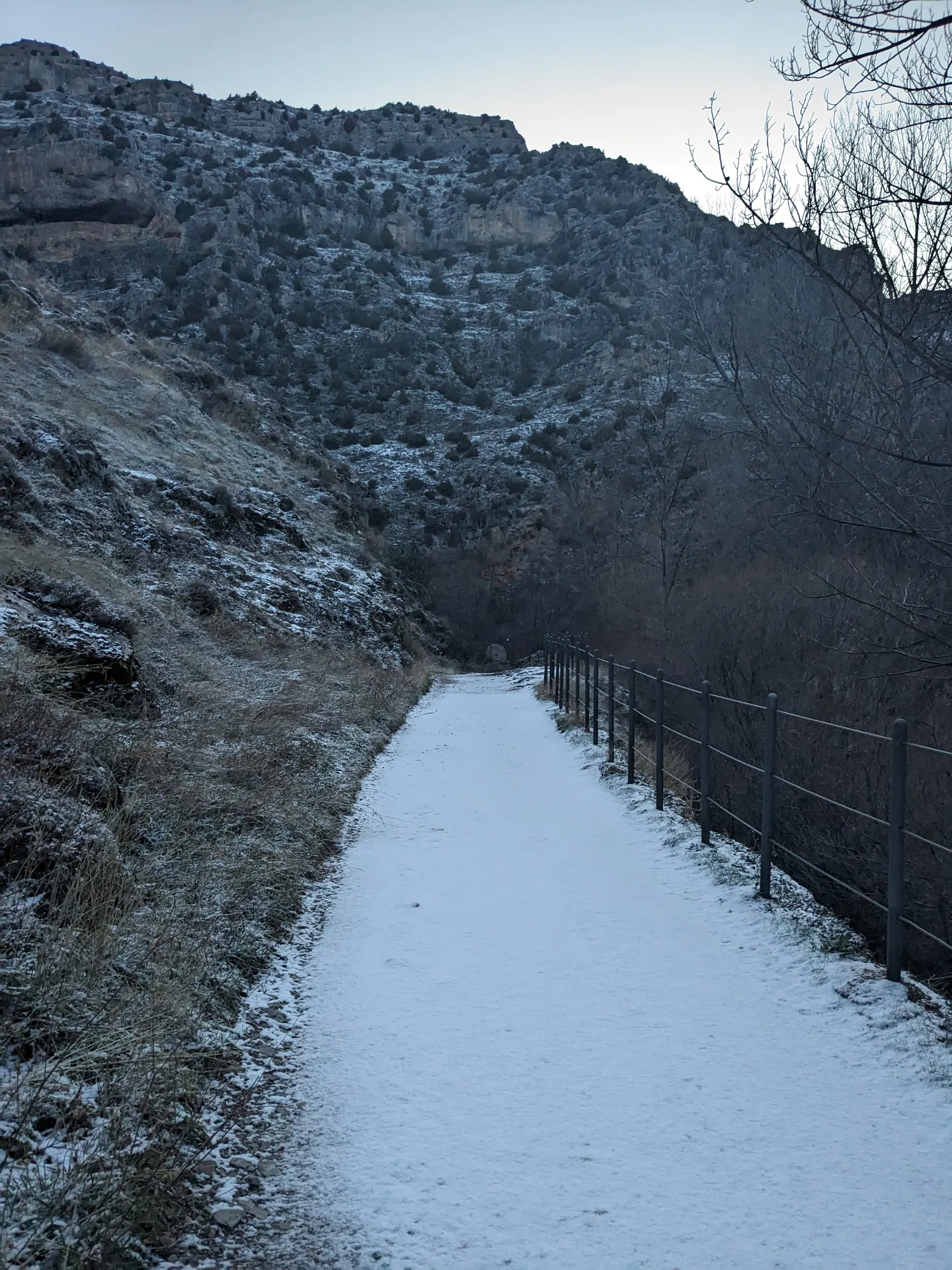 A snow-covered walking path with wooden railings along the Guadalaviar river gorge below Albarracín