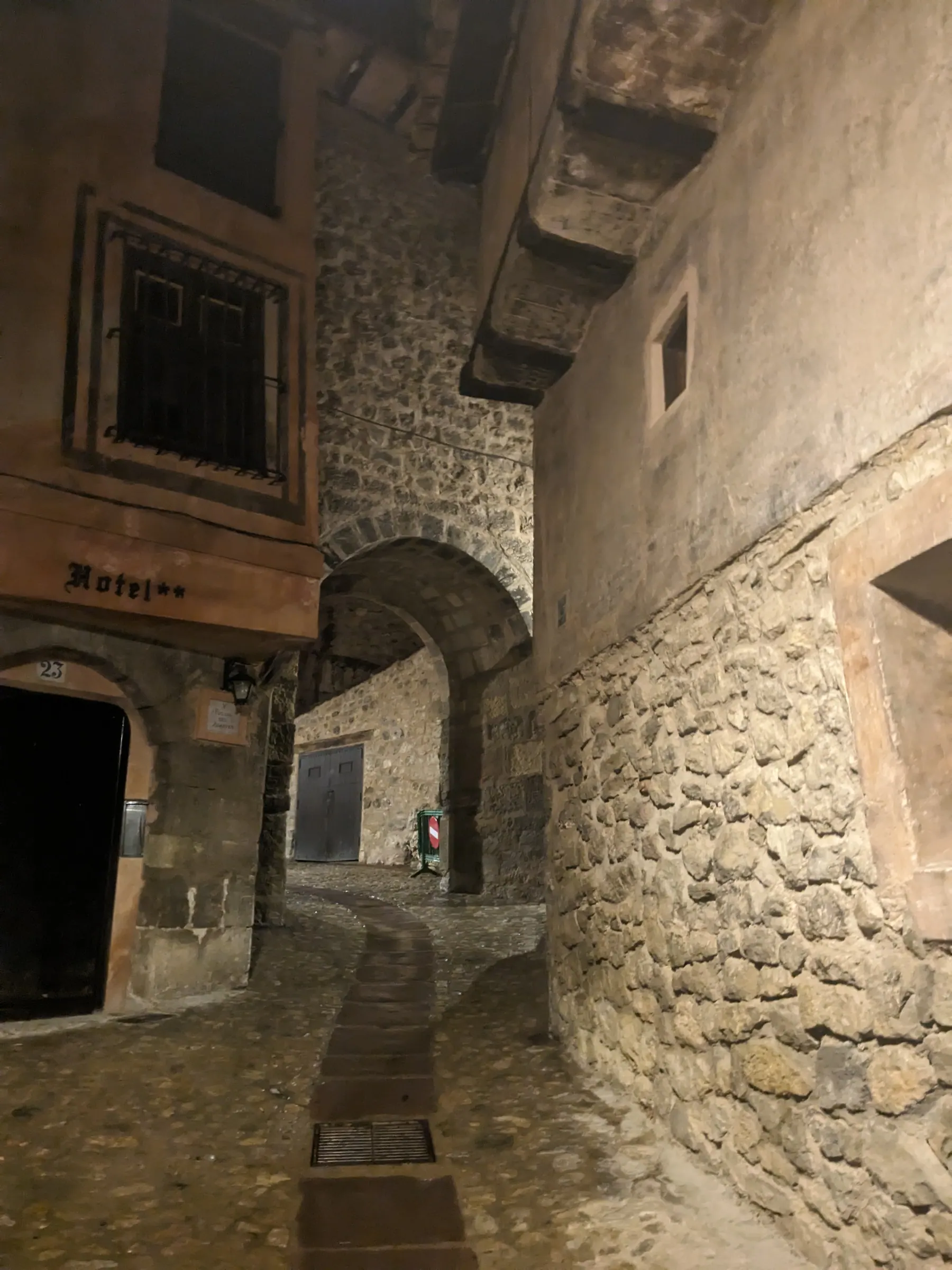 A quiet cobblestone alley in Albarracín illuminated by street lamps under a low stone arch tunnel at night