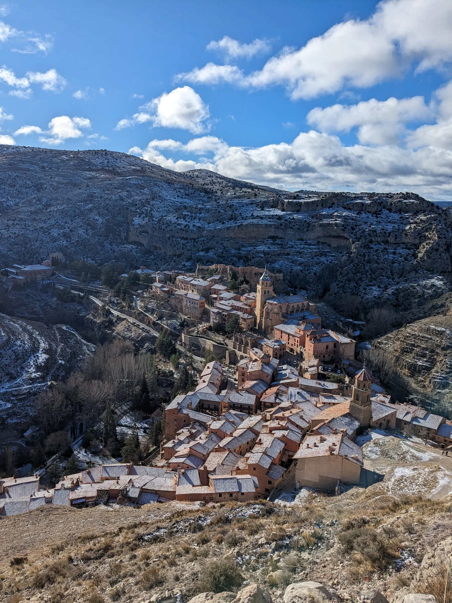Elevated view from the stone fortress walls looking down over the snow-dusted tiled roofs and church tower of Albarracín