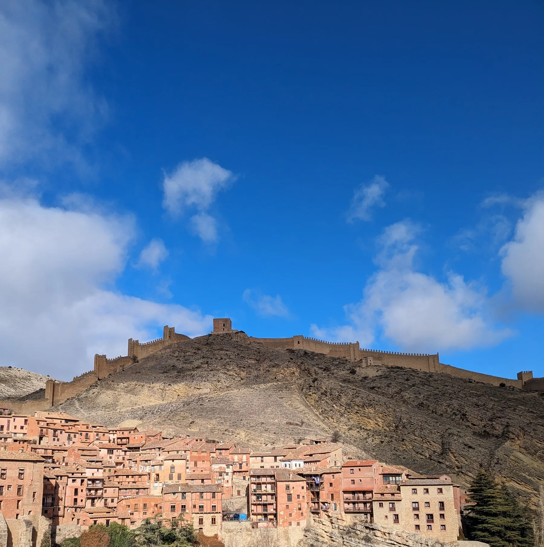 Medieval fortress walls and towers stretching along the mountain ridge above the village houses of Albarracín under a blue sky