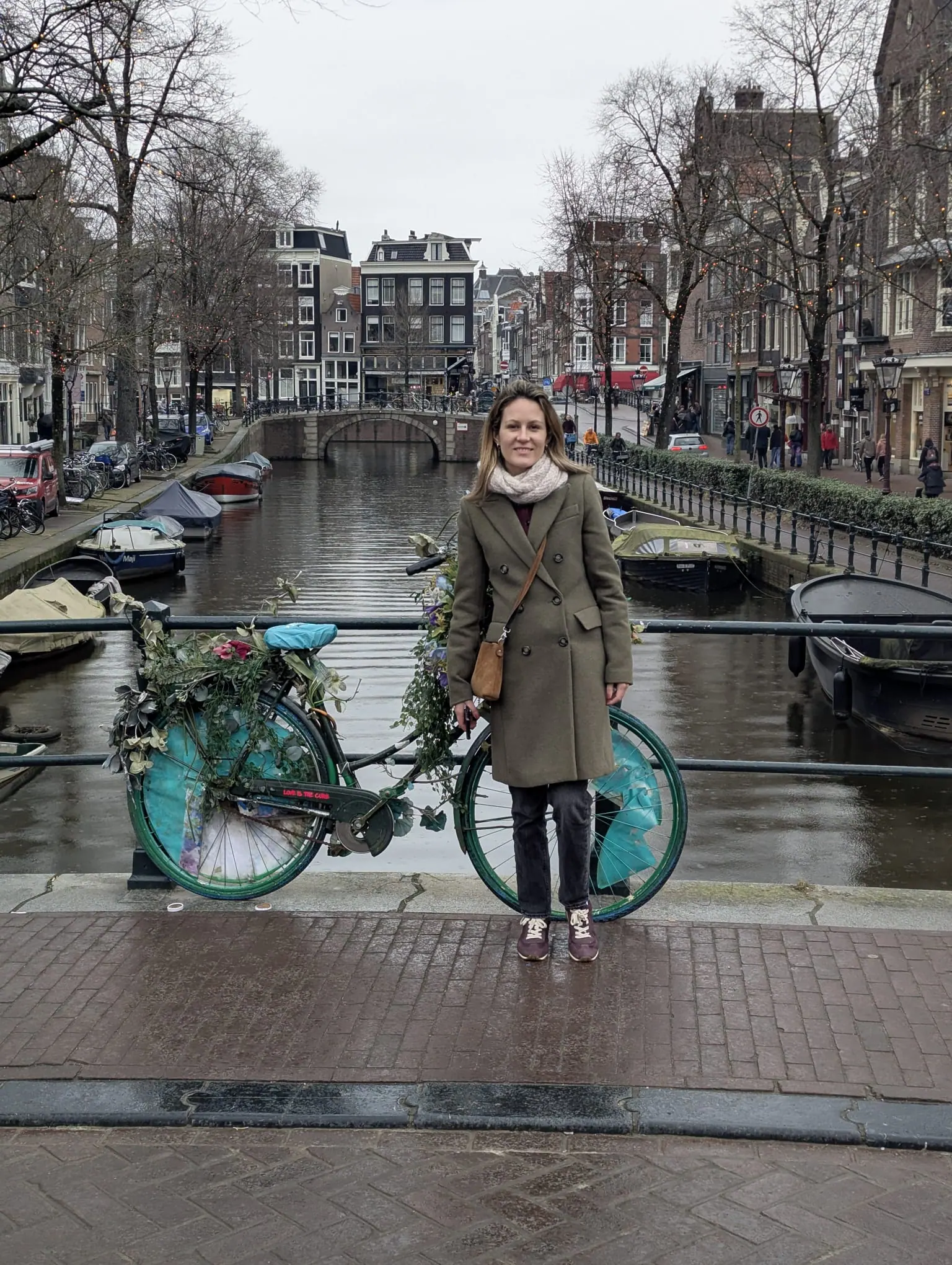 A traveler standing on an Amsterdam canal bridge beside a decorated bicycle