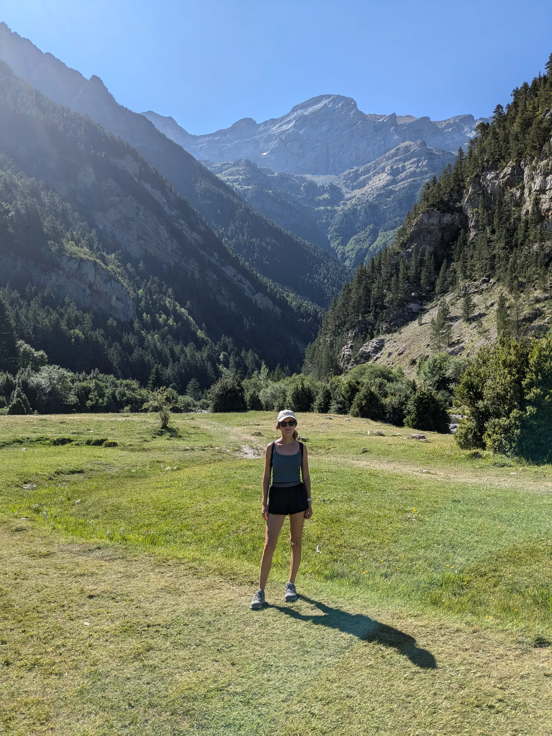 A hiker standing in a broad green valley beneath the mountains of Ordesa