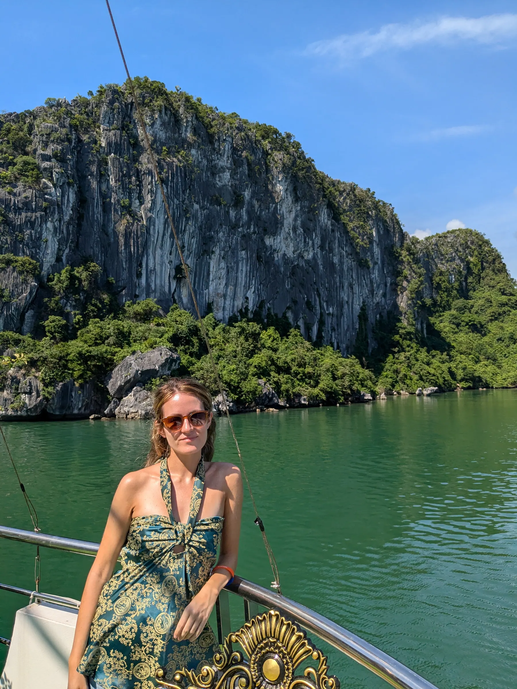 Zane standing on a boat in front of a towering limestone cliff above green water in Lan Ha Bay