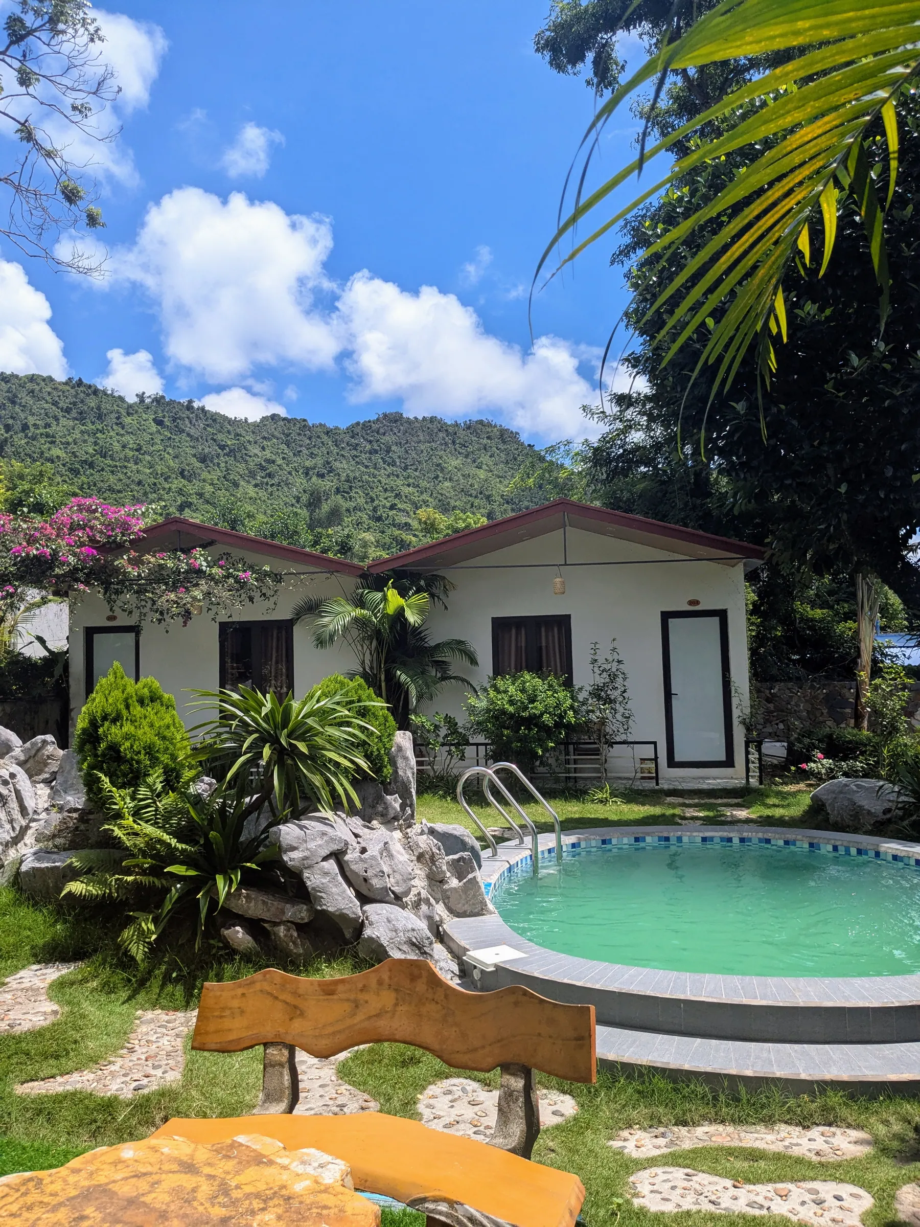 A swimming pool surrounded by palm trees and small bungalow houses at Tran Chau Garden Home in Cat Ba