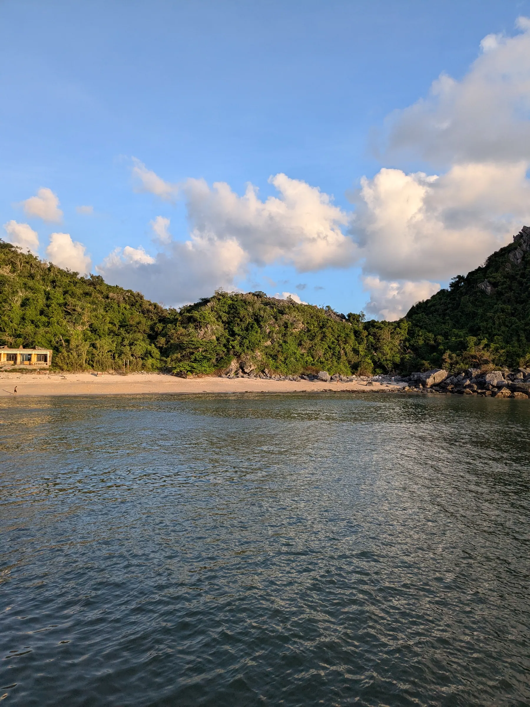 A wooden tour boat cruising near the limestone cliffs and sandy shore of Monkey Island in Lan Ha Bay