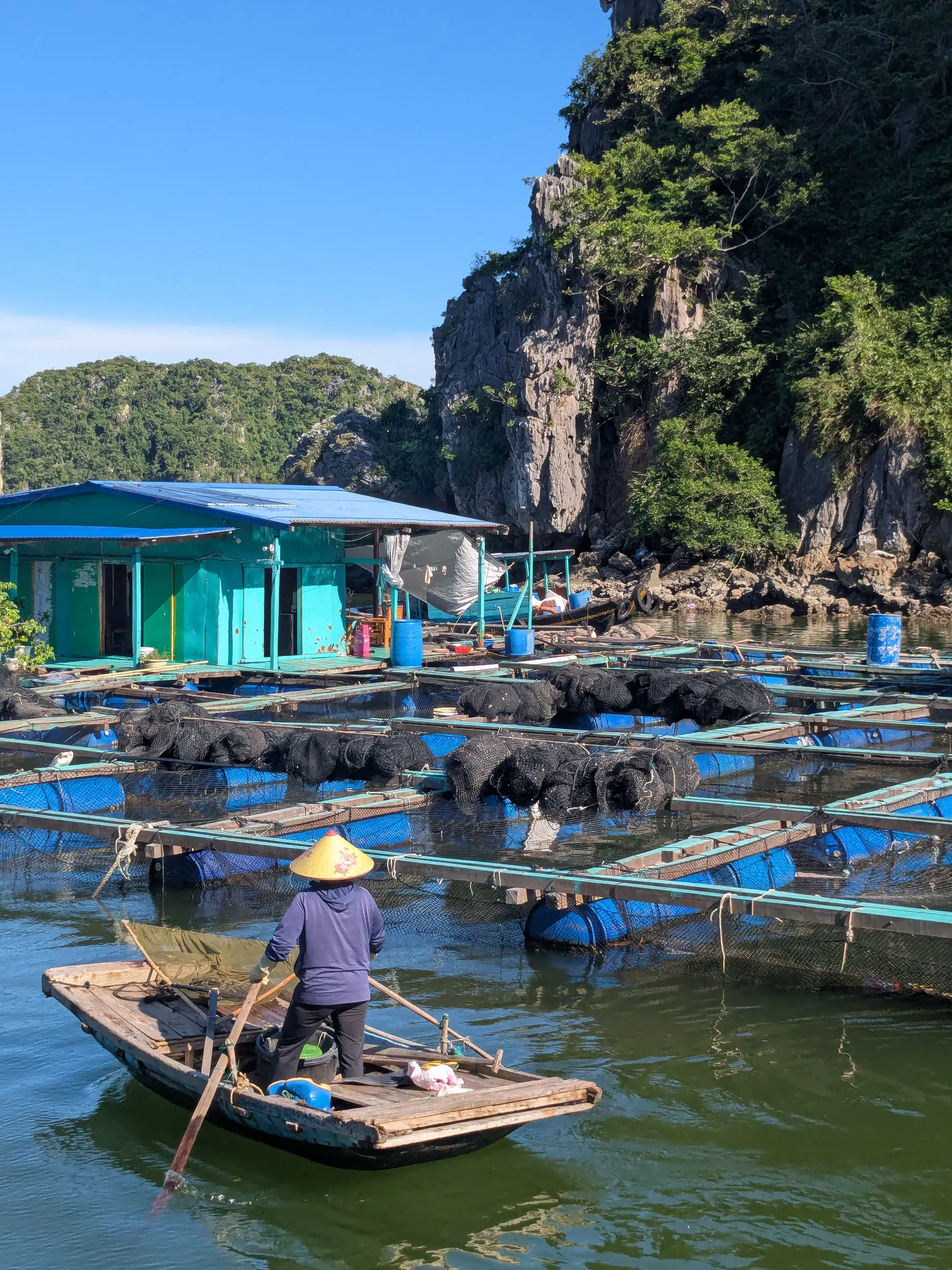 Floating wooden houses, fishing nets, and rafts moored beneath giant limestone walls in Lan Ha Bay