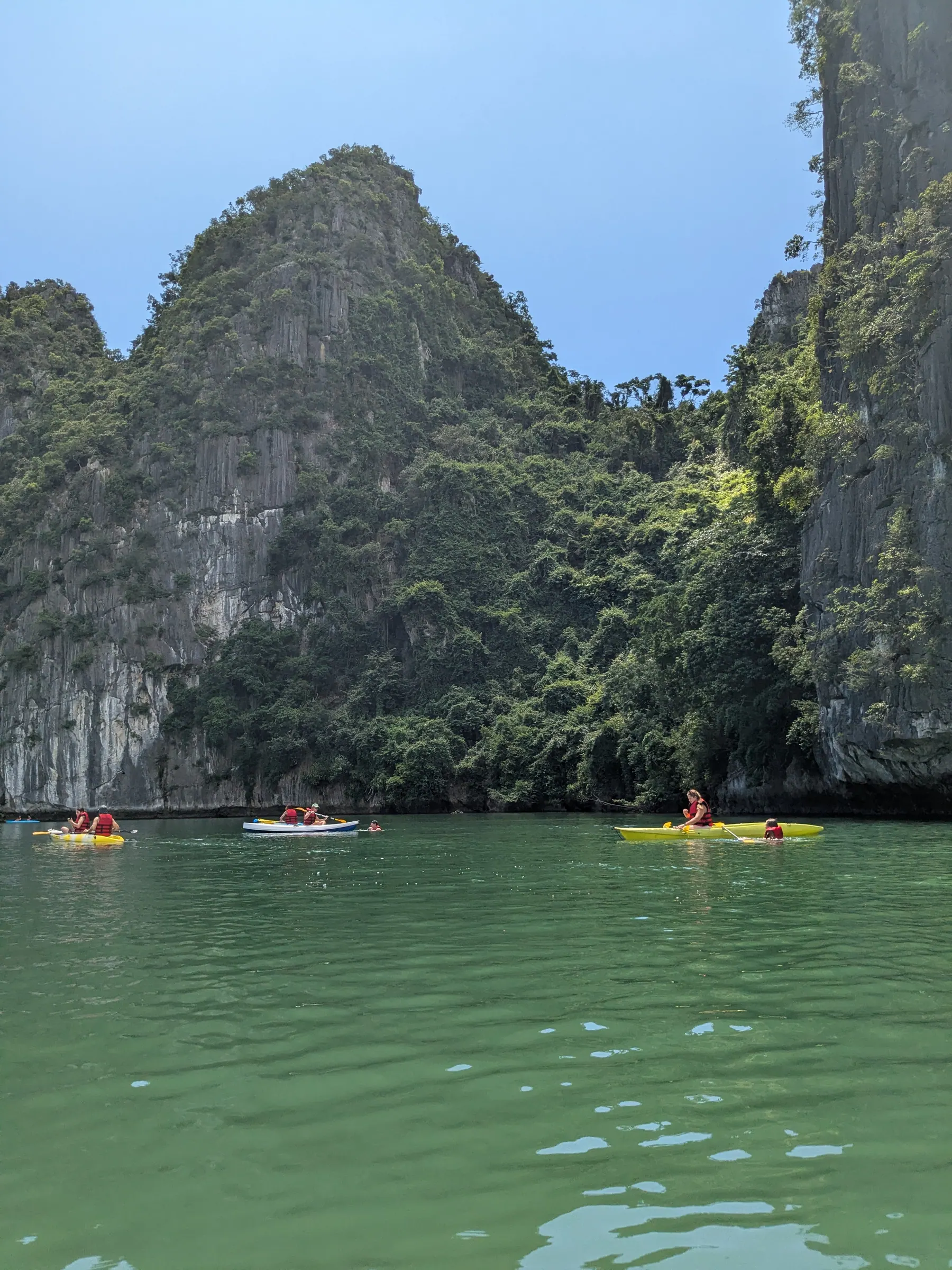 Brightly coloured kayaks heading toward a low natural rock archway in Lan Ha Bay