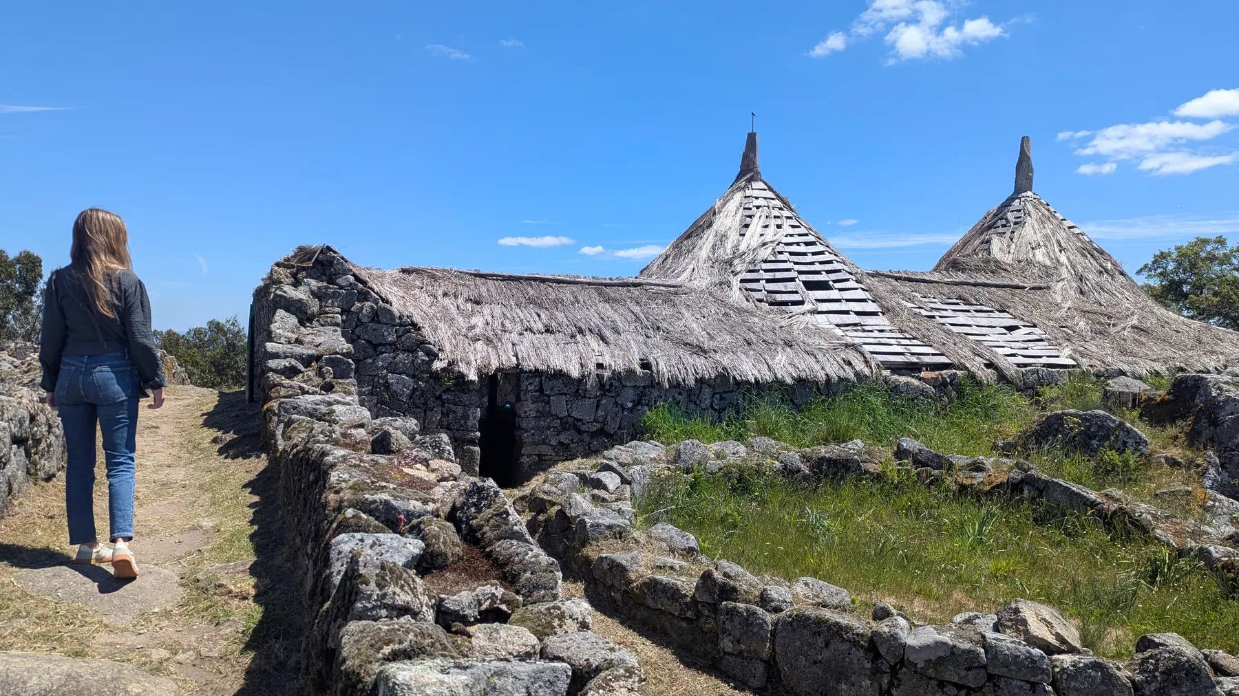 A traveler walking beside reconstructed stone huts at Citânia de Sanfins