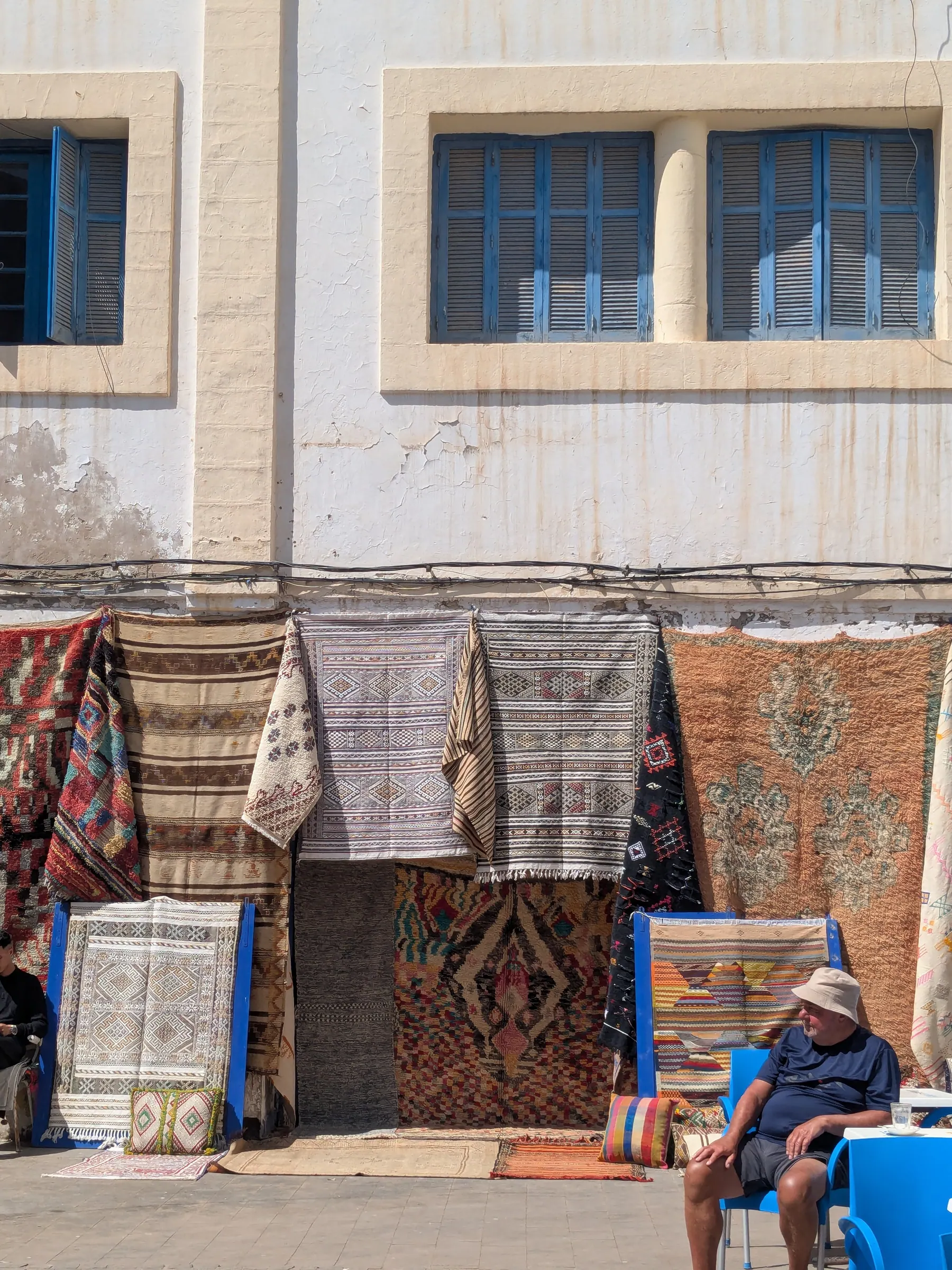 Rugs displayed against a white and blue building in Essaouira