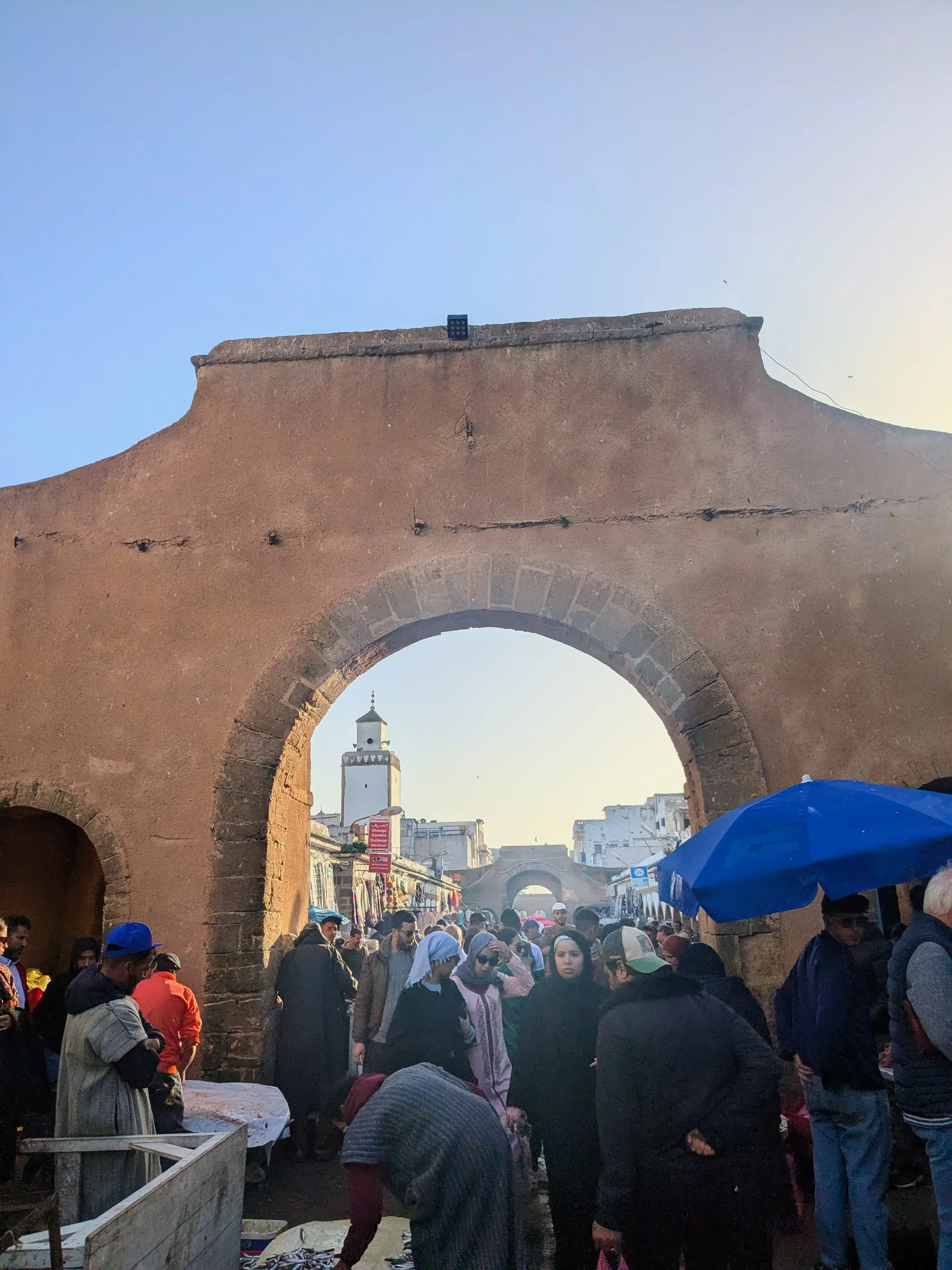 A crowded market gate in Essaouira with a minaret visible through the arch