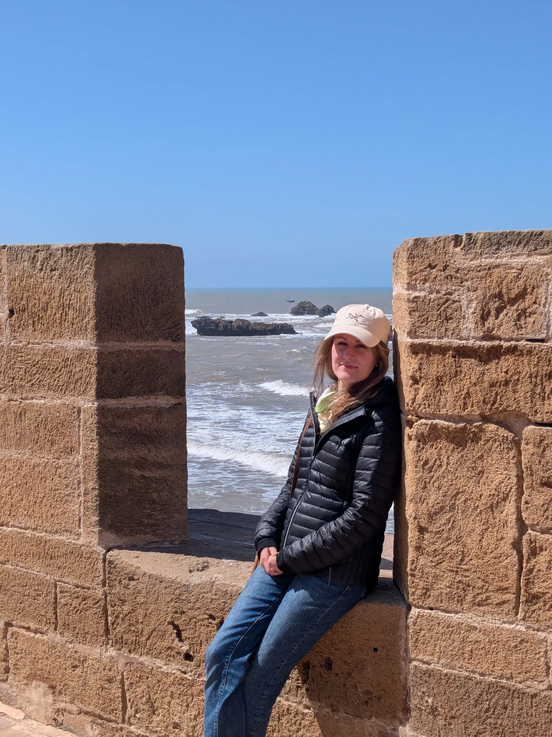 A traveler sitting on Essaouira's sea ramparts with waves behind her