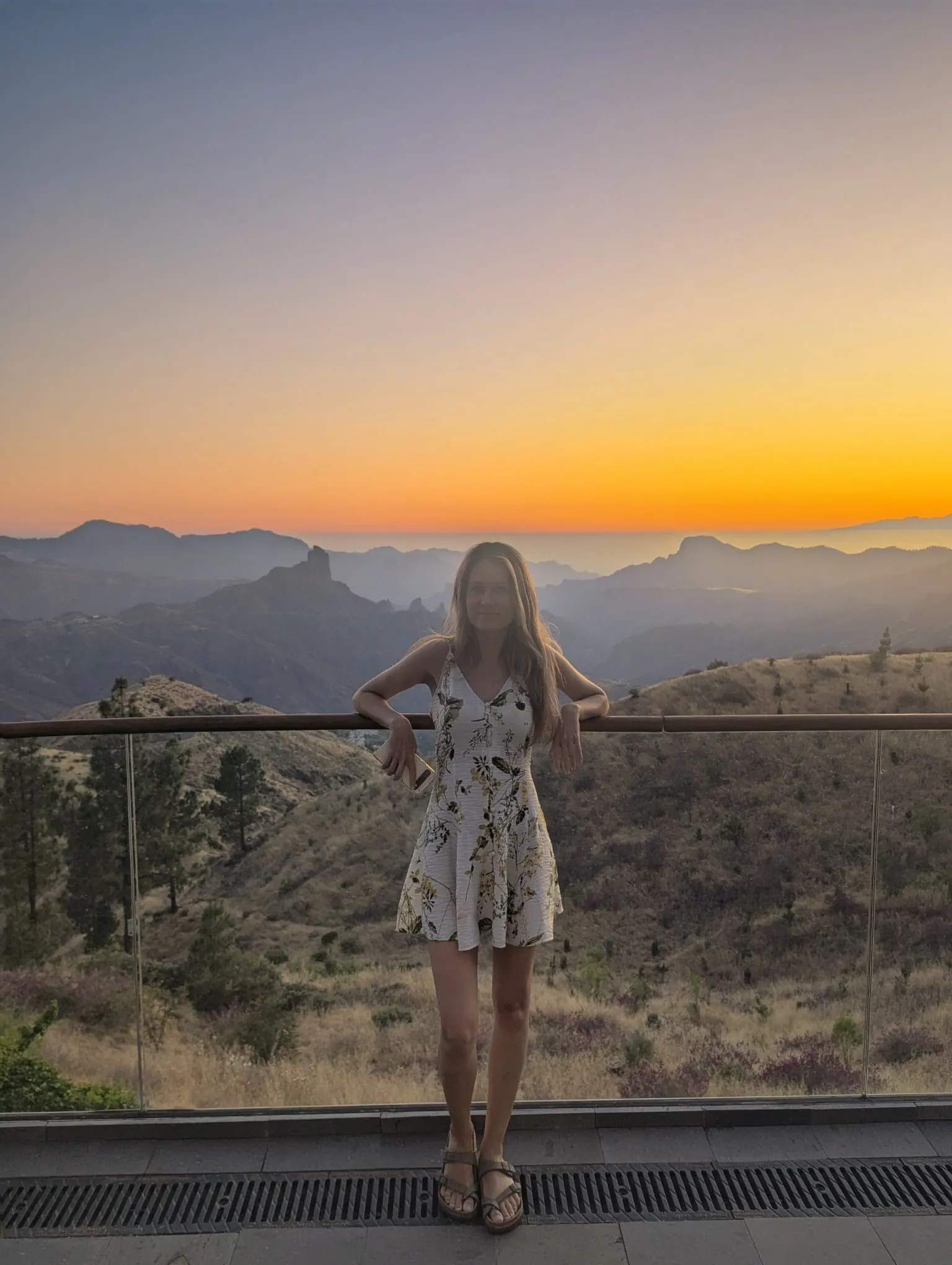 A traveller standing on a terrace at sunset with layered Gran Canaria mountains behind her