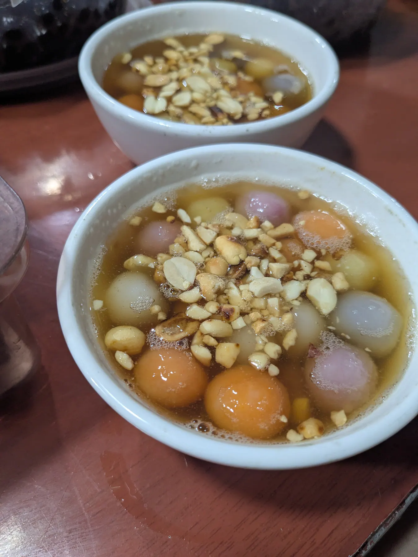 Two bowls of coloured rice balls in syrup topped with chopped nuts in Dong Van