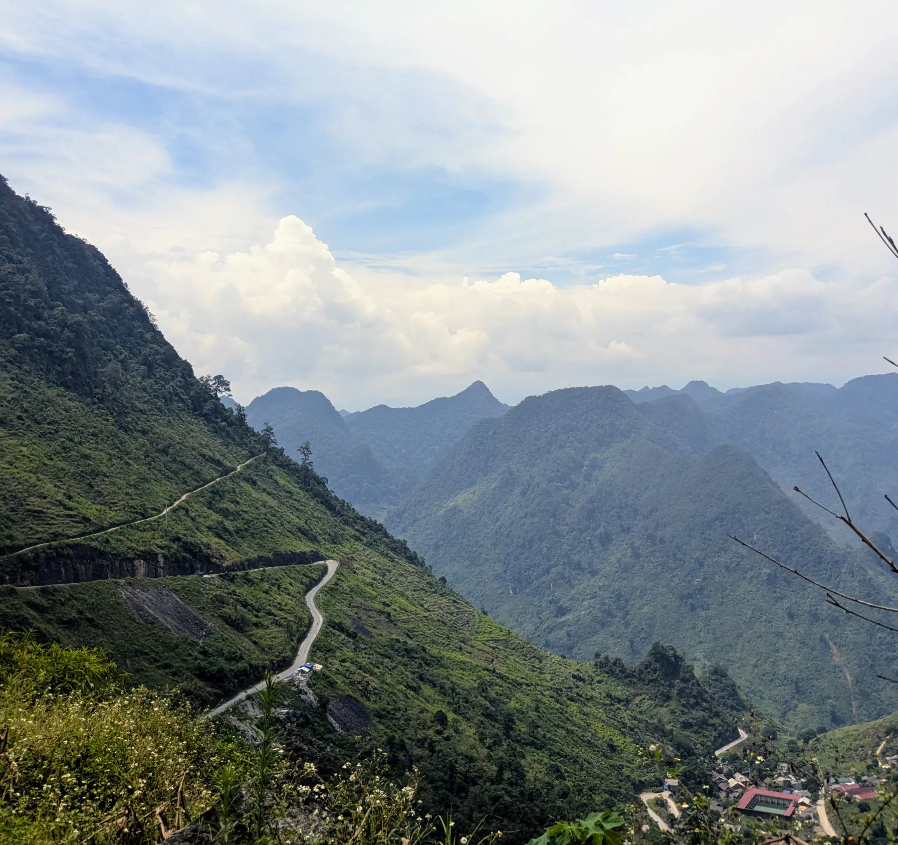 A narrow road zigzagging across a green mountainside above a village on the final day of the Ha Giang loop