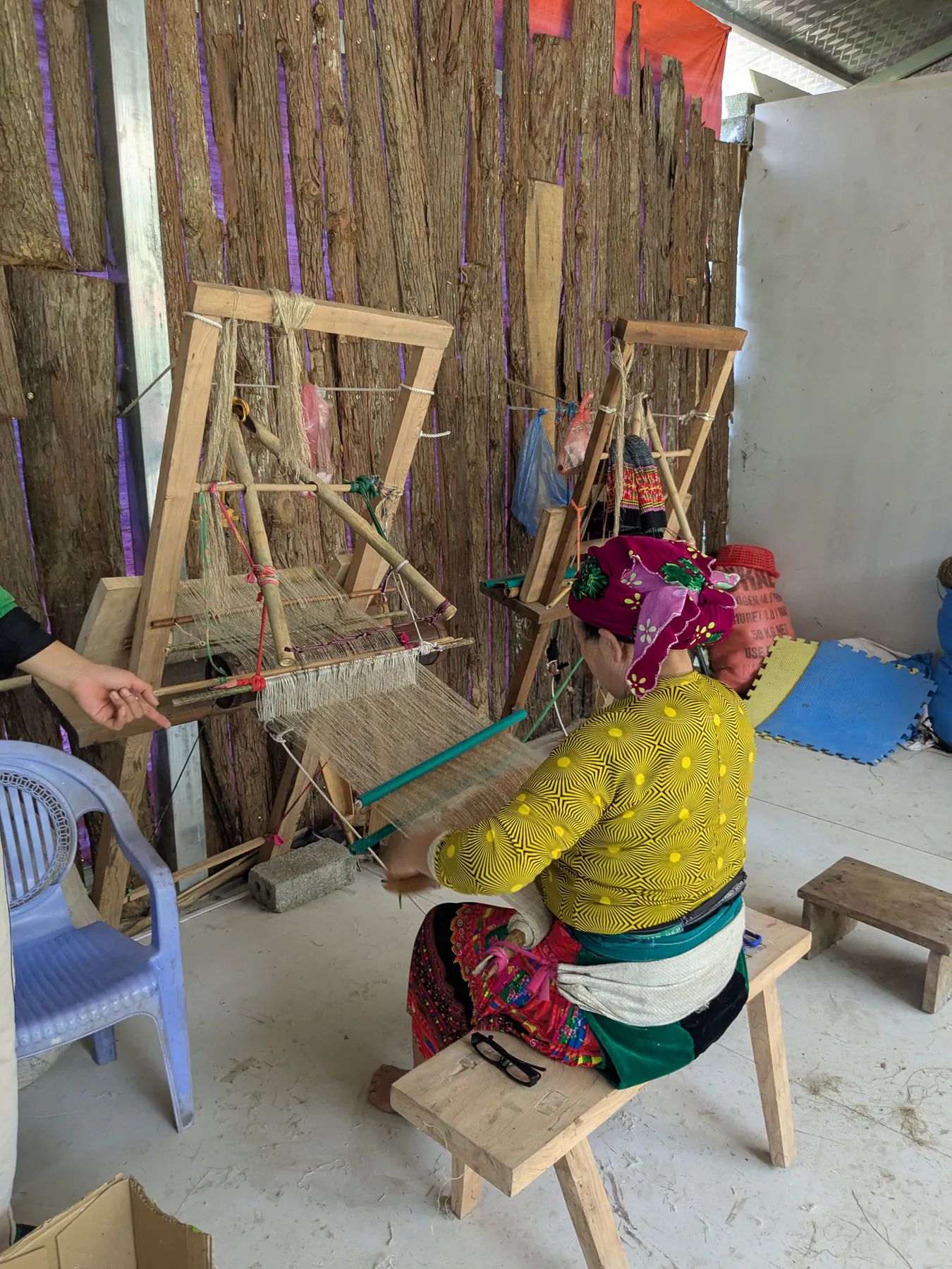 A woman in a patterned headscarf working at a wooden loom in a hemp workshop on the Ha Giang loop