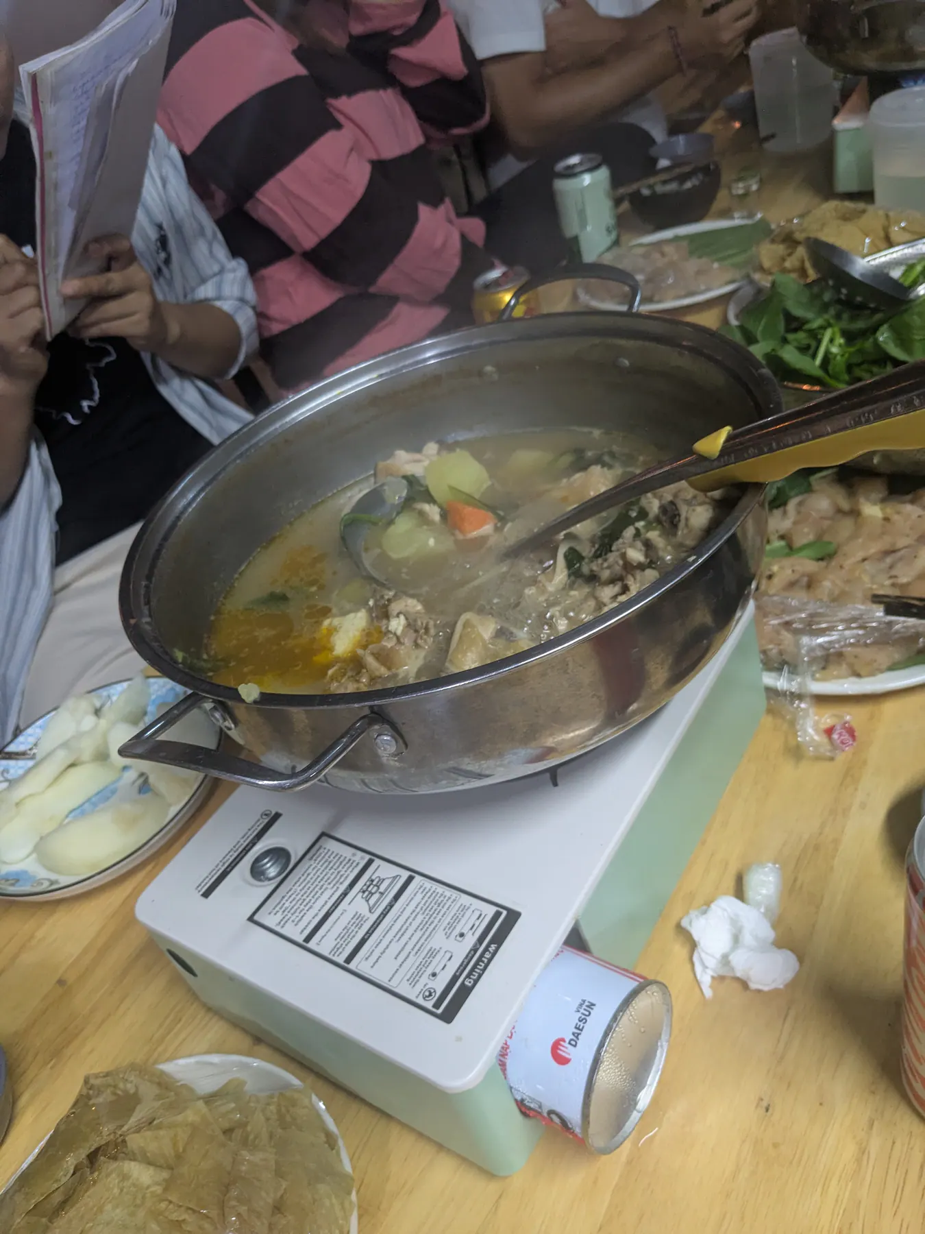 A steaming metal hotpot on a portable stove surrounded by ingredients at dinner in Dong Van