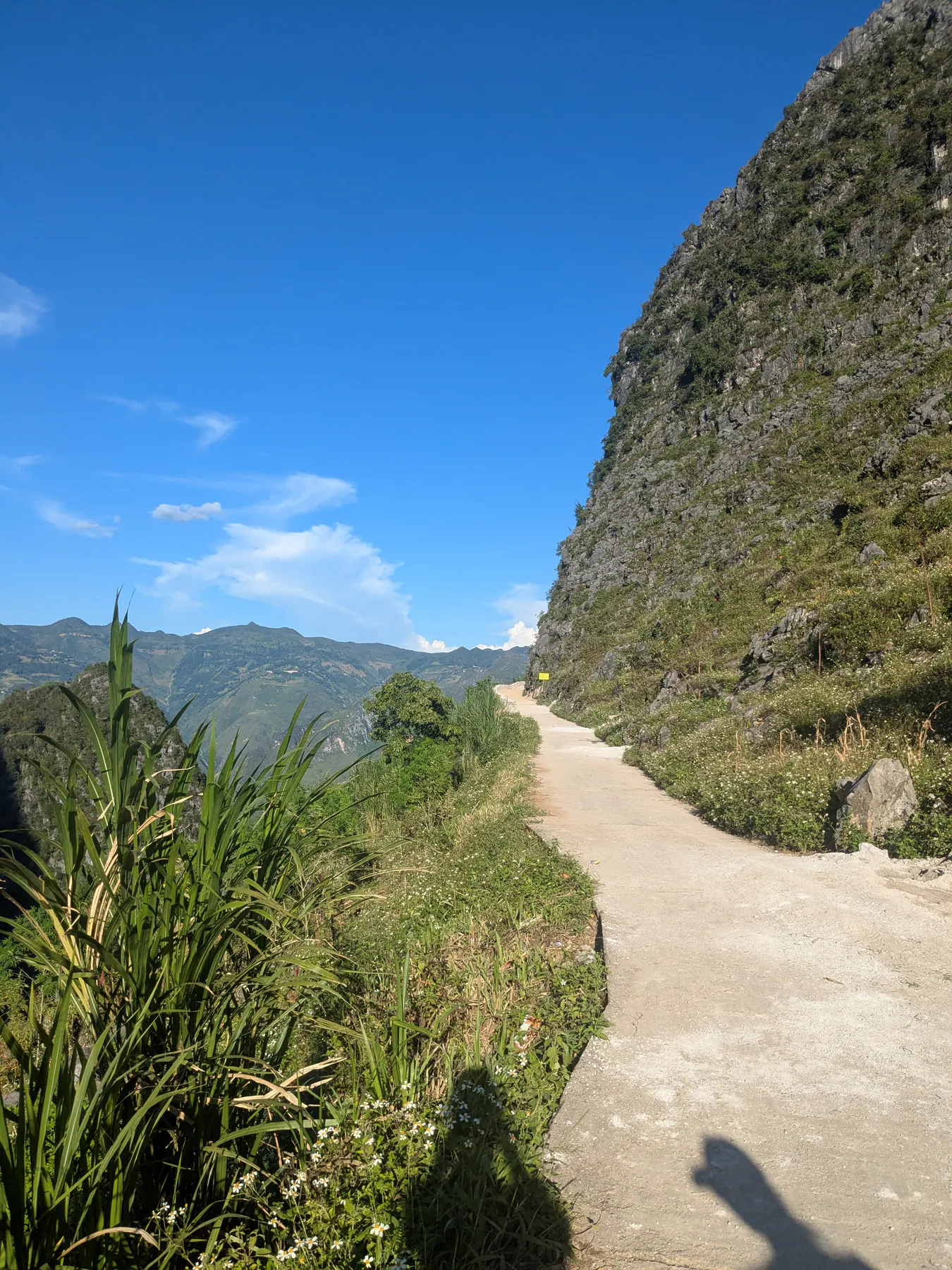 A pale footpath climbing beside a rocky cliff and tall grass above Ma Pi Leng pass