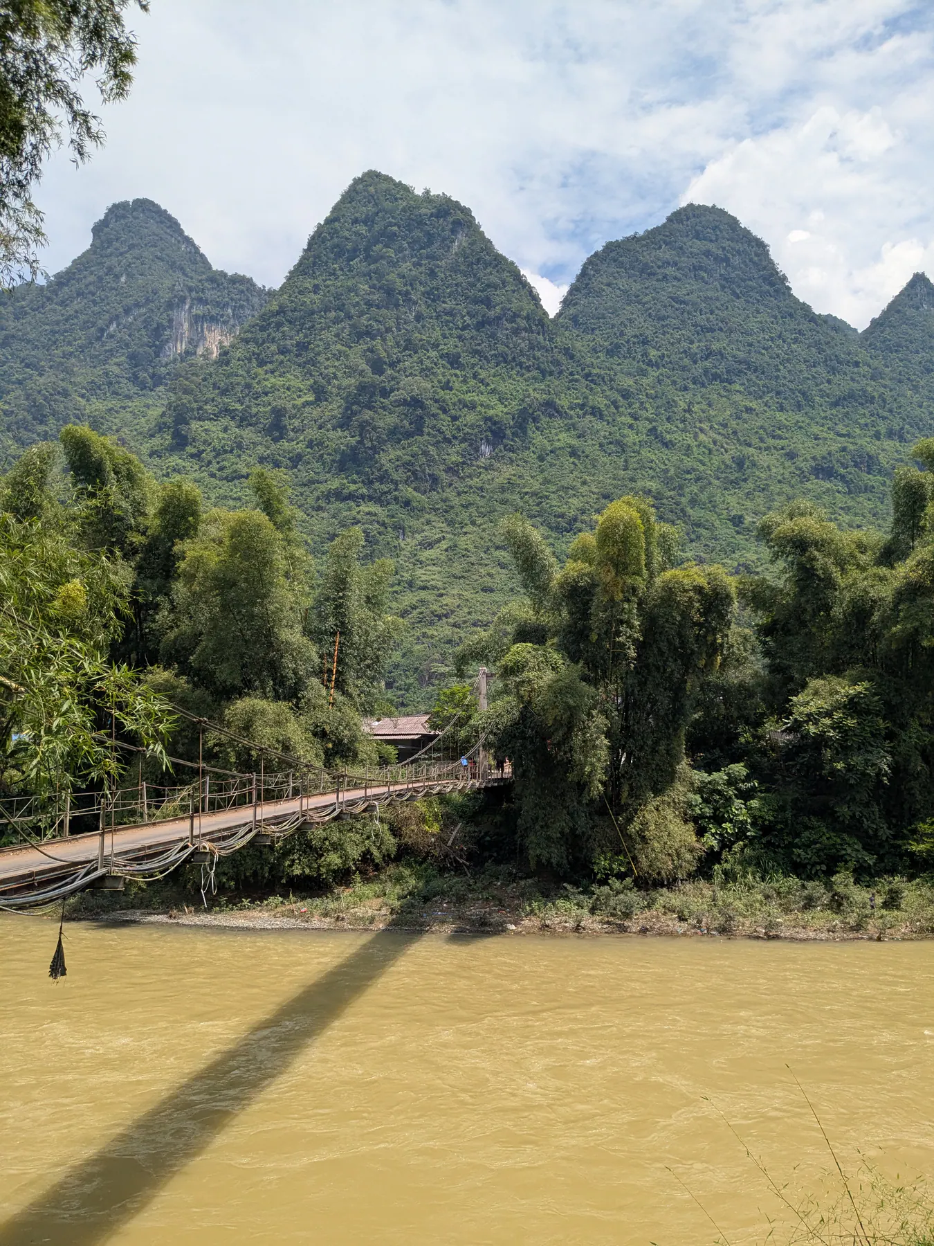A suspension bridge spanning the brown Song Lo River beneath green limestone peaks