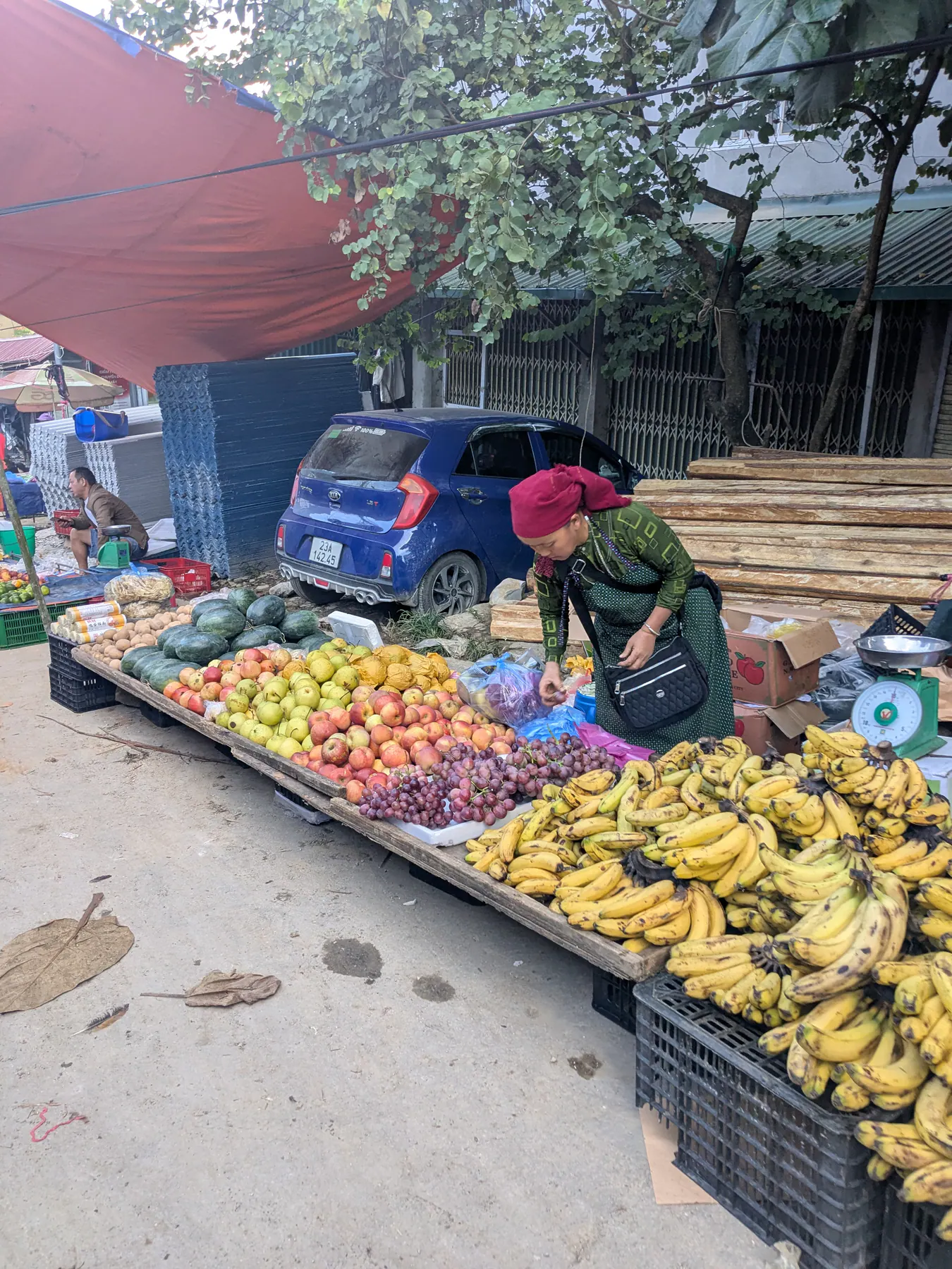 A woman seated beside baskets of bananas and other fruit under an umbrella at Dong Van market