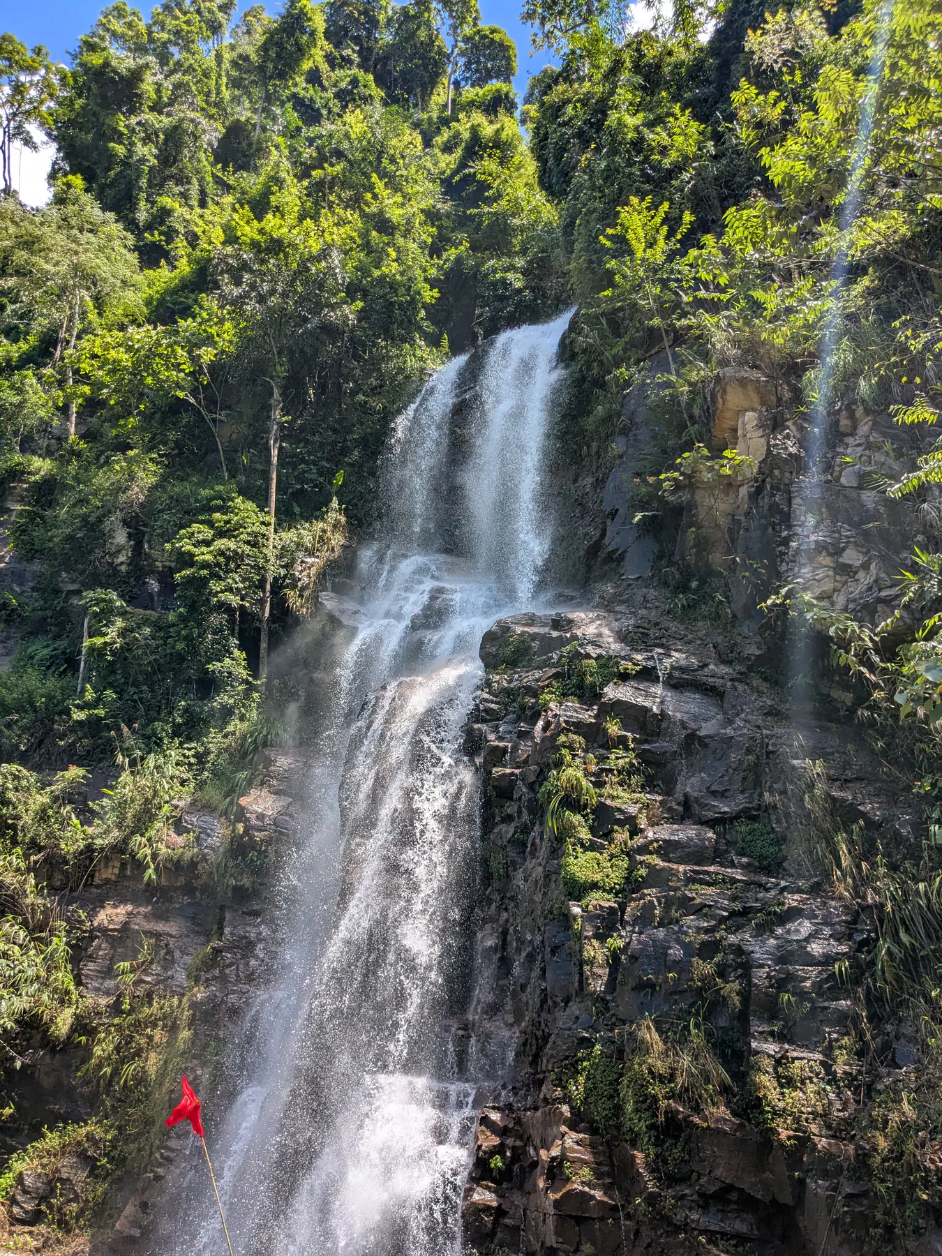 A Boong waterfall spilling in several white streams over dark rocks surrounded by greenery