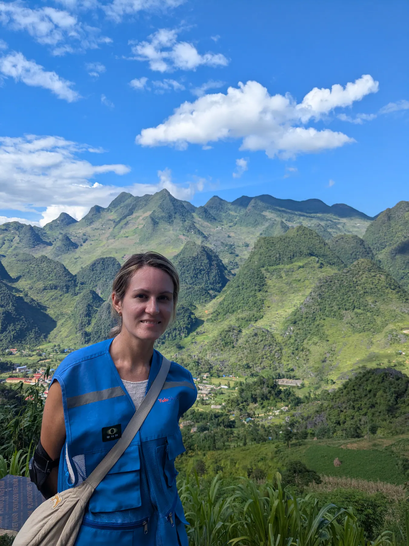 A traveller wearing a blue shirt in front of layered green mountains near Lung Ho