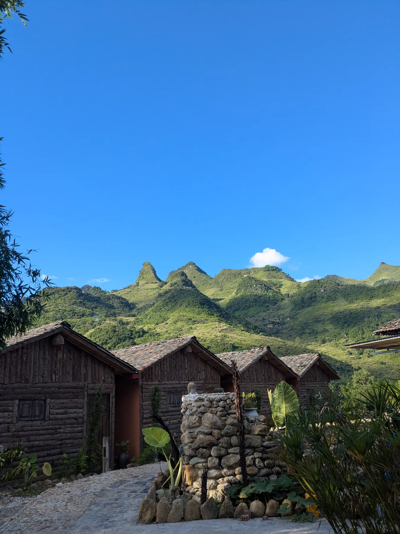 Wooden guest cabins lining a path beneath grassy hills at Du Gia Panorama Ecolodge