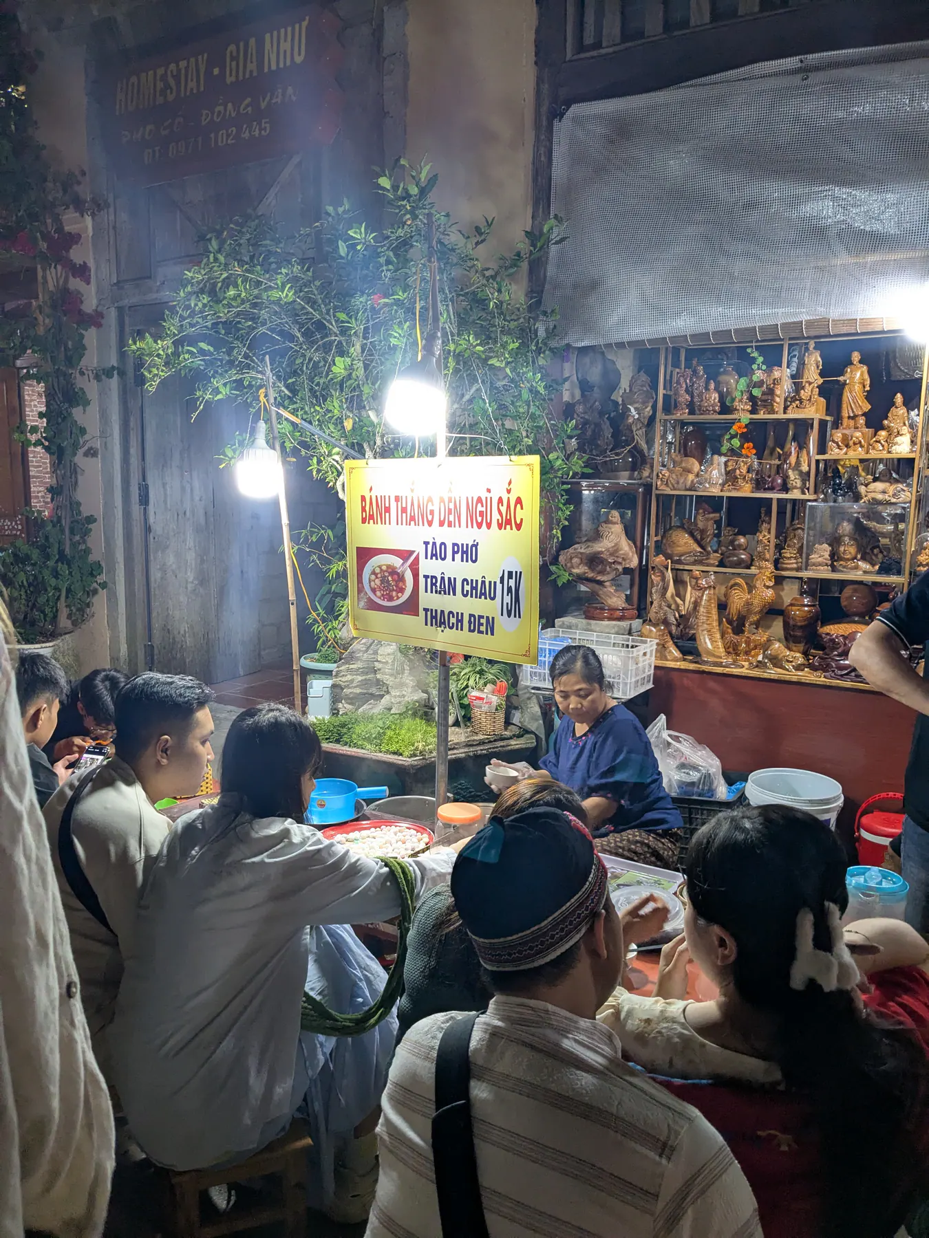 Diners seated at low tables beside a lit street-food stall at night in Dong Van