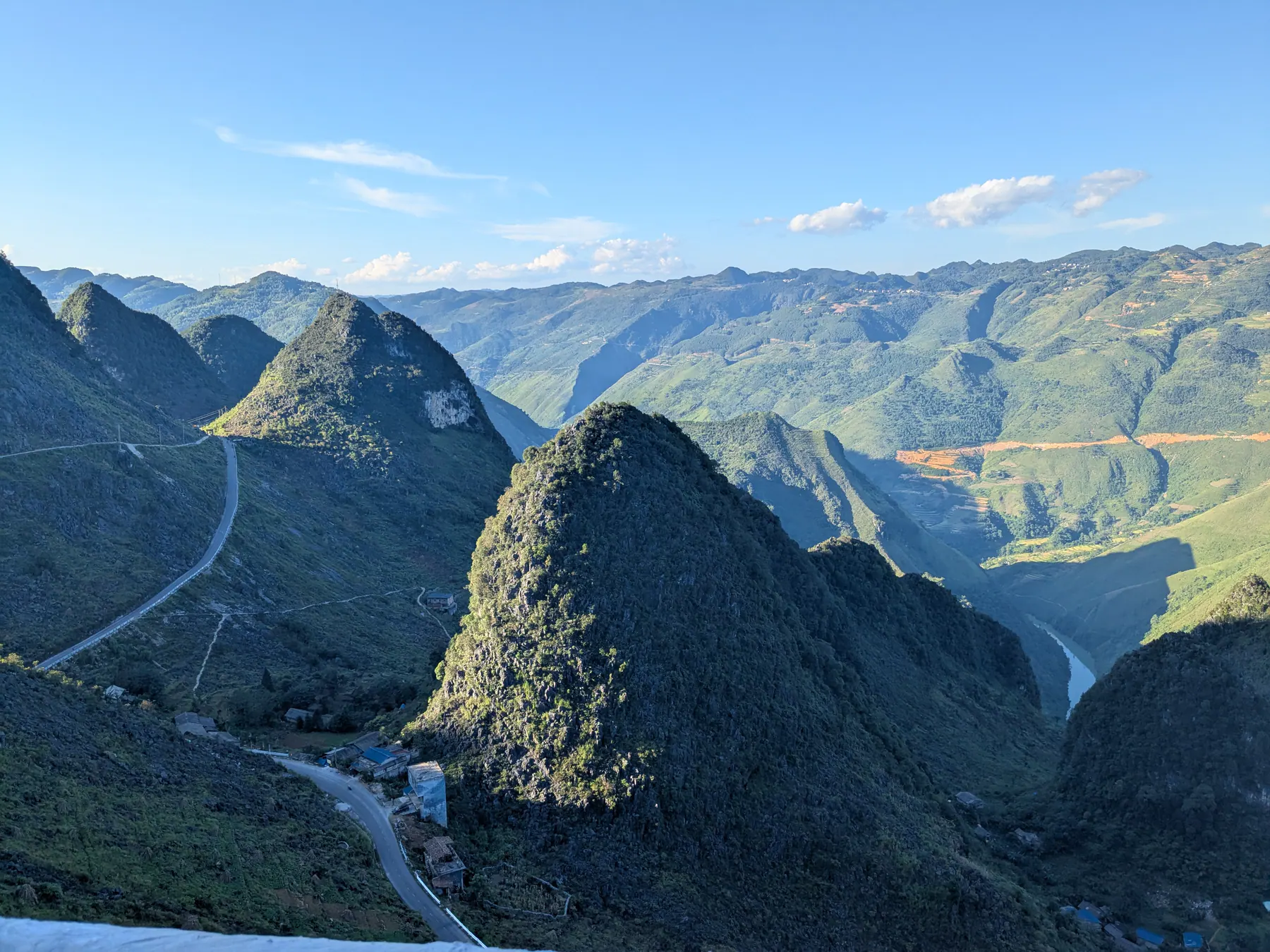 Roads bending around a steep conical peak with layered mountains beyond Ma Pi Leng