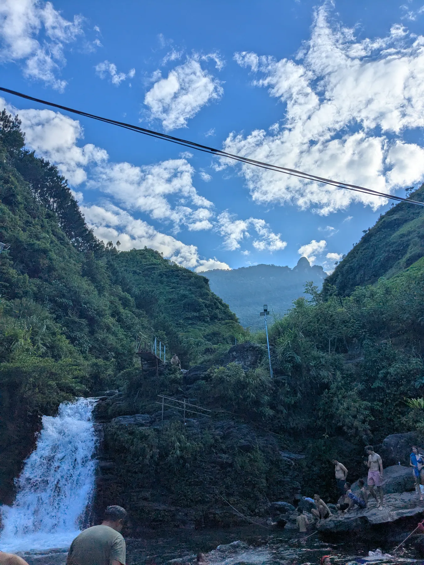 Du Gia waterfall falling into a rocky pool beneath wooded slopes and a narrow overhead bridge