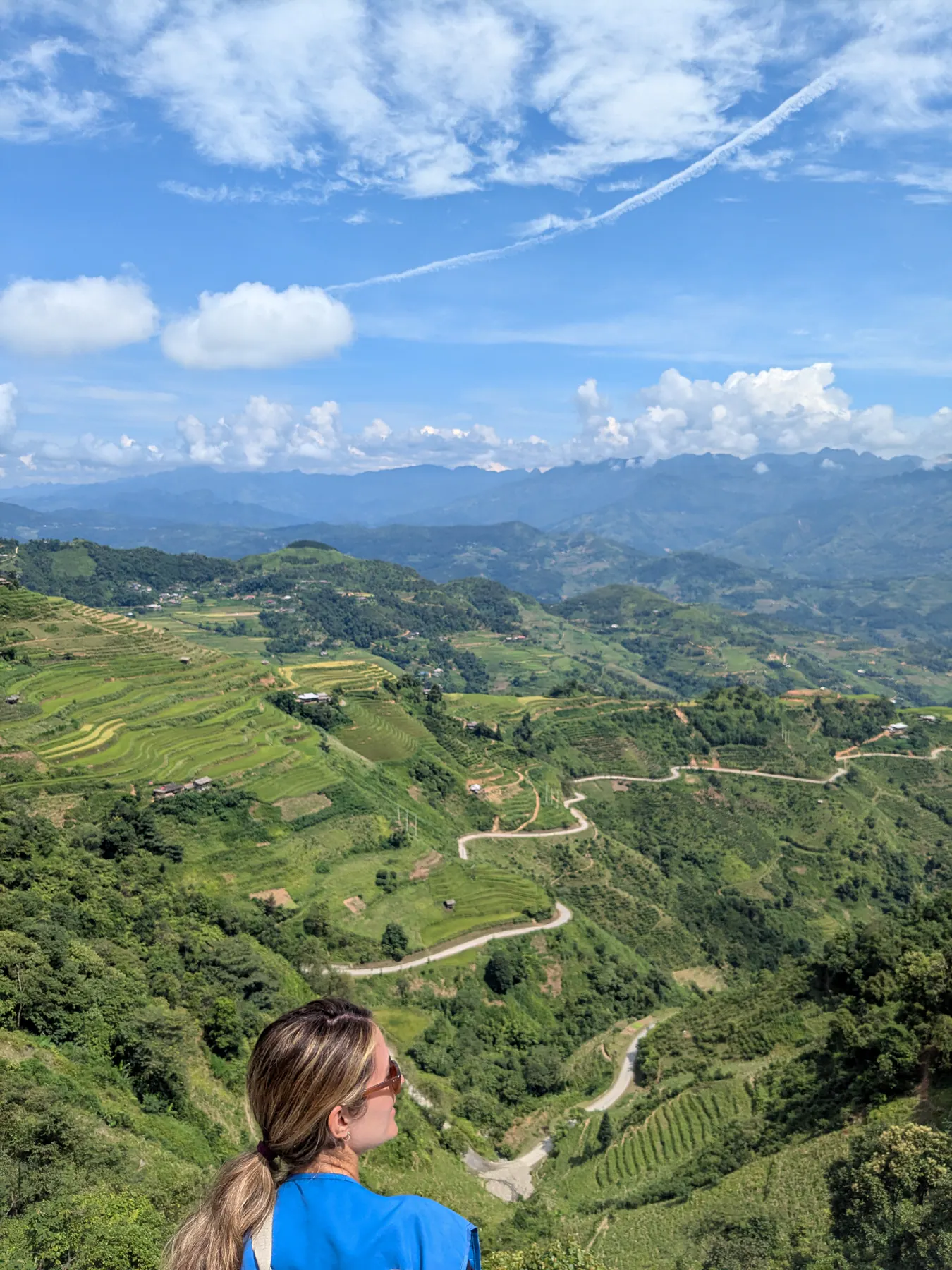 A traveller looking over terraced green hills and a winding pale road near Mau Due