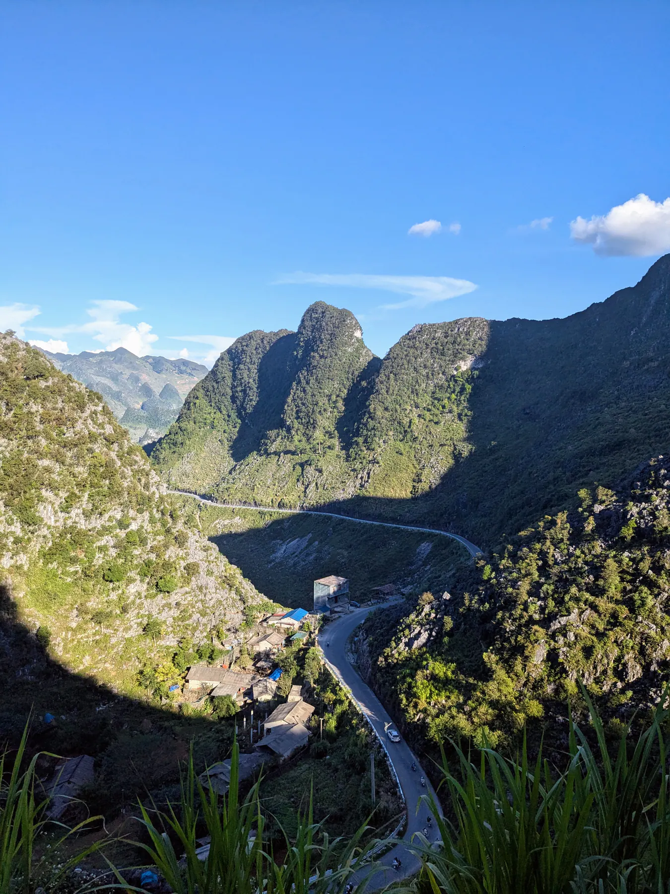 A mountain road winding between steep green peaks beneath a vivid blue sky near Ma Pi Leng
