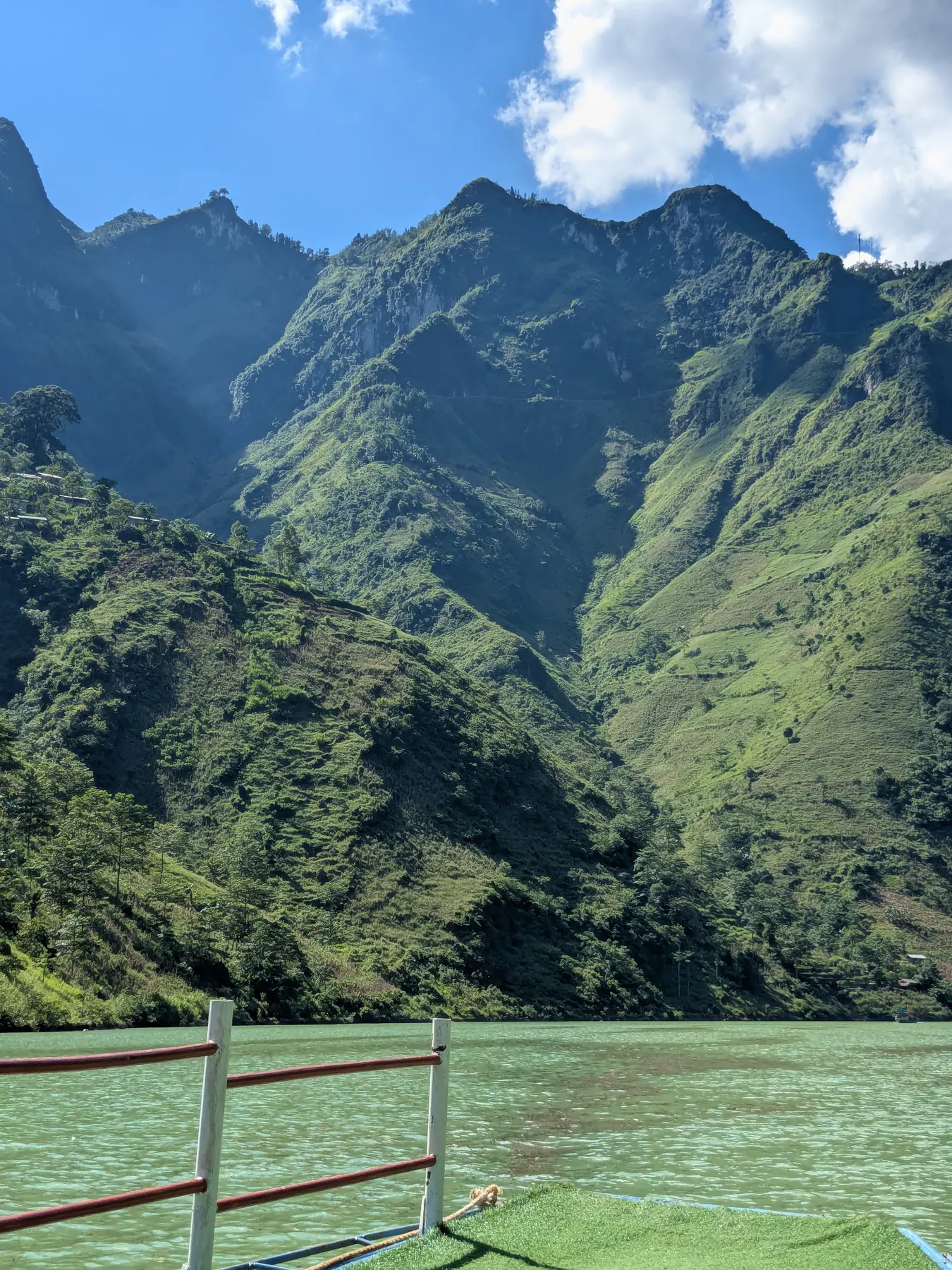 Green Nho Que river water and towering forested canyon walls seen over a boat railing