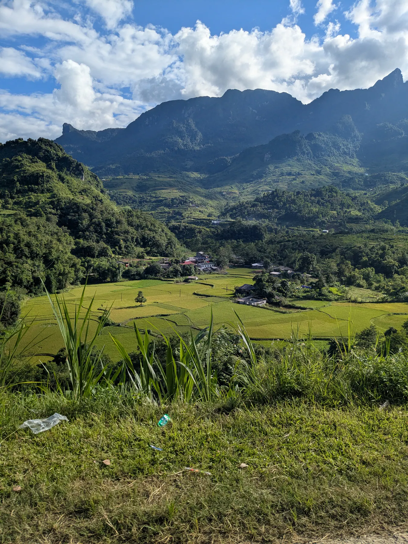 Sunlit rice fields and scattered village houses beneath a line of jagged green mountains in Ha Giang