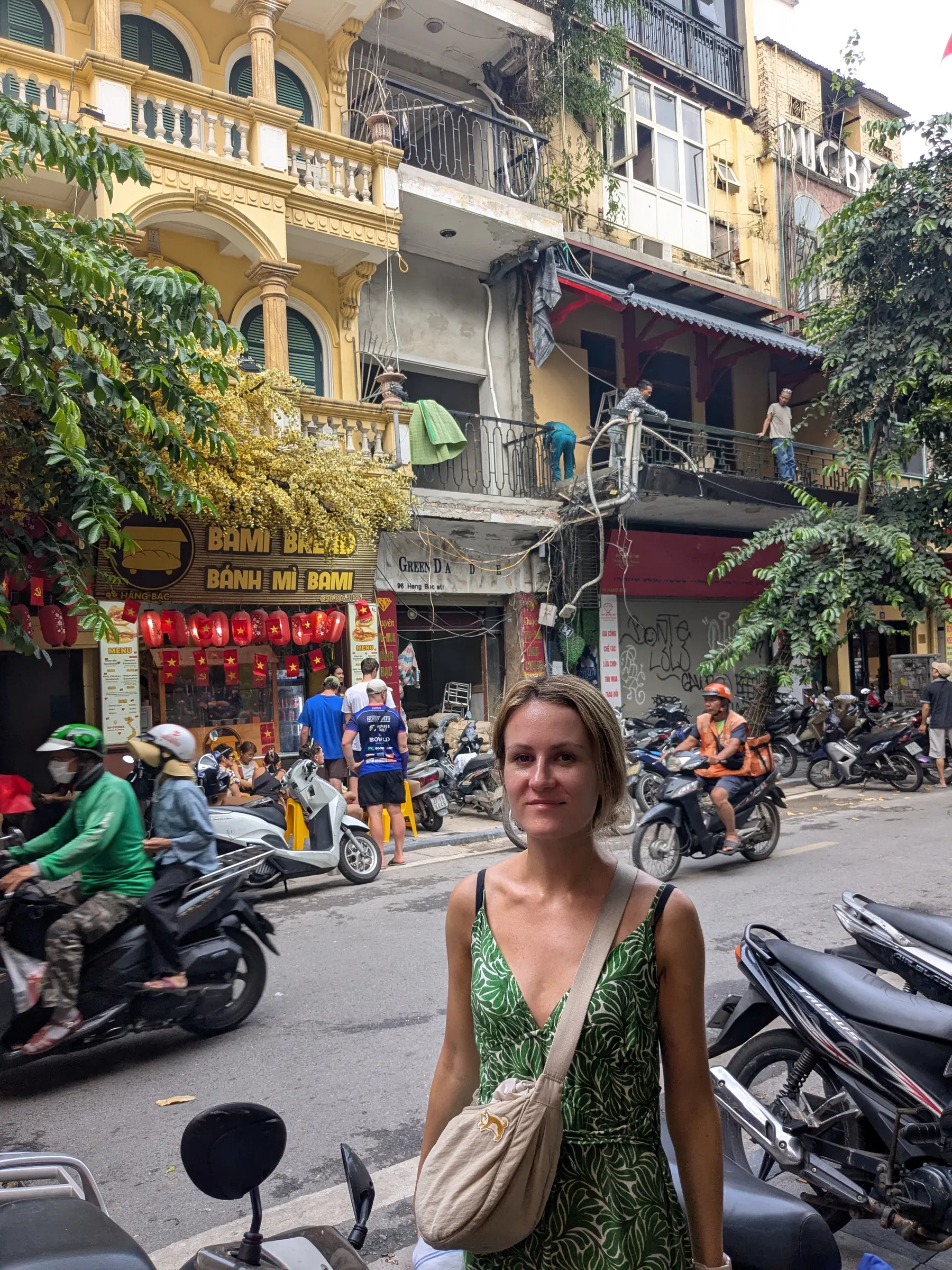 A traveller standing on a Hanoi street beside parked motorbikes and a café