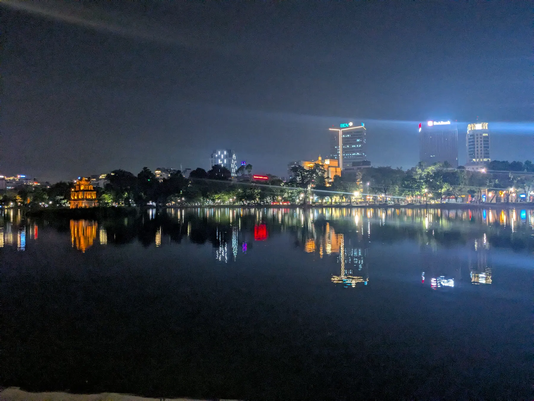 A wide evening view across Hoan Kiem Lake with city lights