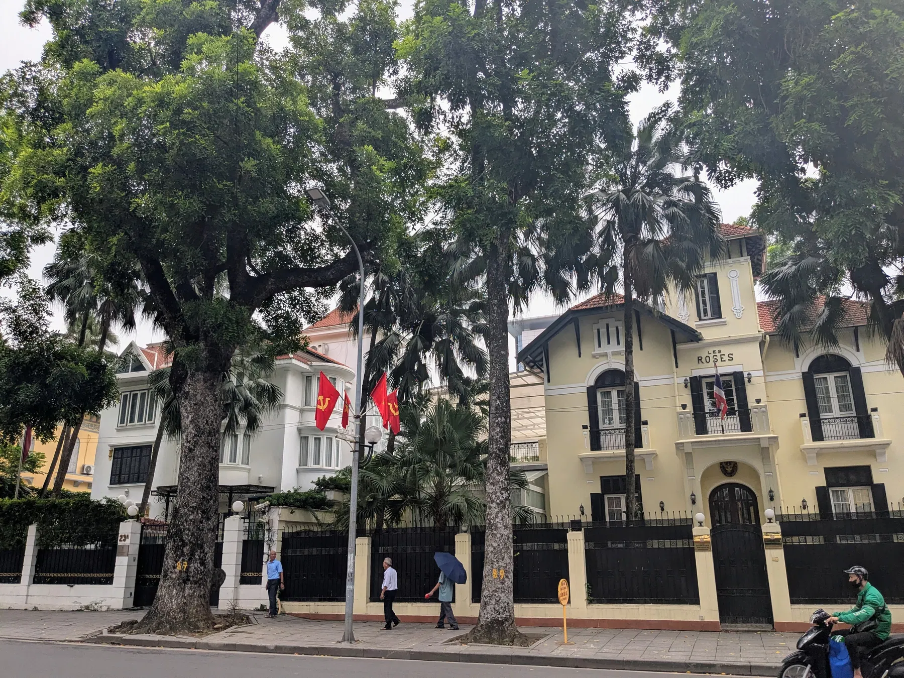 A pale French-colonial building behind mature trees in Hanoi
