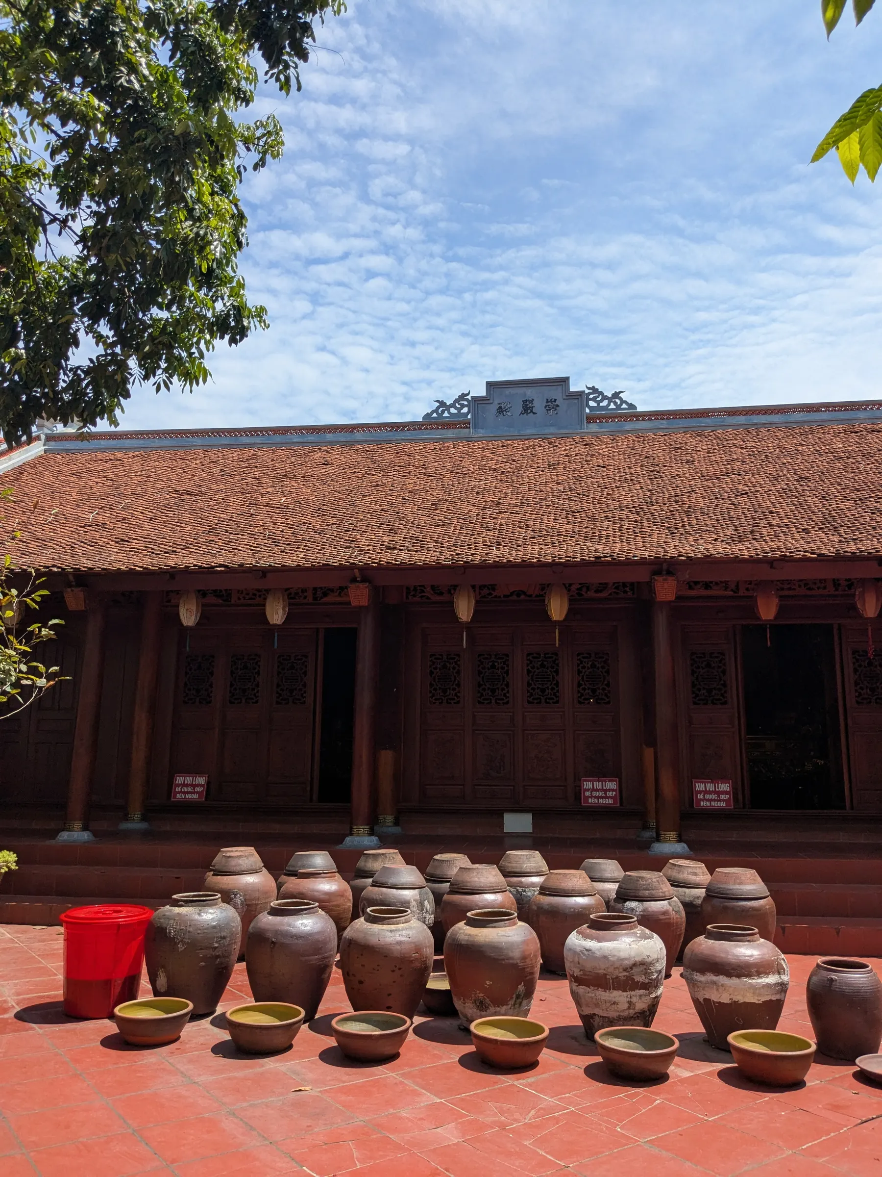 Traditional ceramic soy sauce jars and shallow earthenware bowls arranged in the sunlit courtyard of a historic house in Đường Lâm Ancient Village
