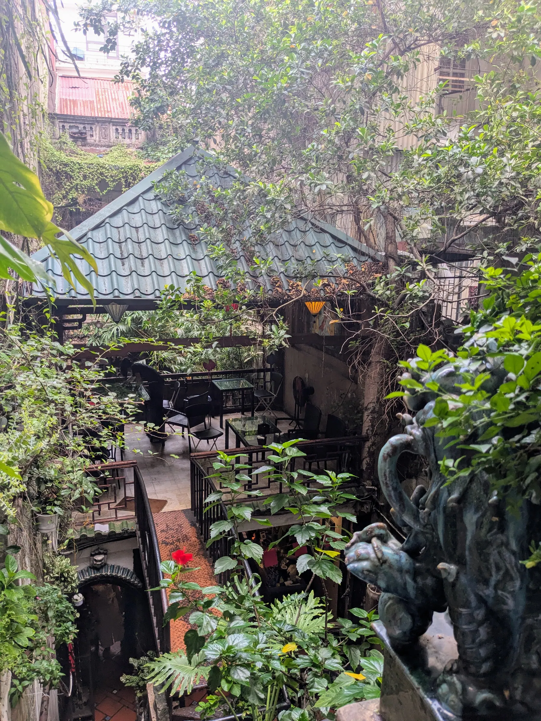 A leafy inner courtyard with a green roof and café tables at Café Phố Cổ in Hanoi