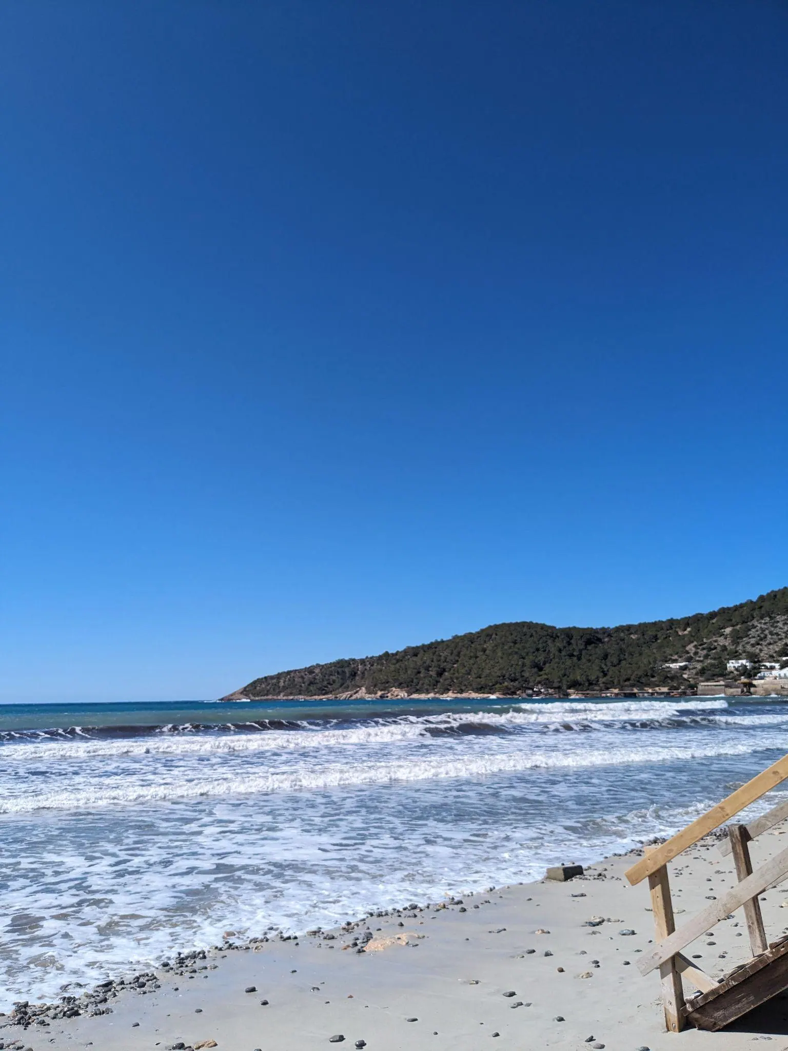 Wooden walkway stairs leading down to Platja de Ses Salines with waves rolling onto the sand