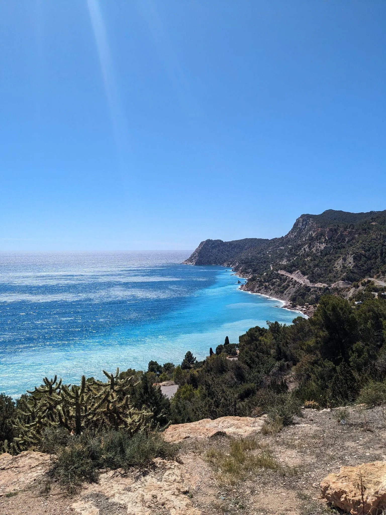 Elevated vantage point overlooking a turquoise Mediterranean bay and rugged green cliffs on the coast of Ibiza