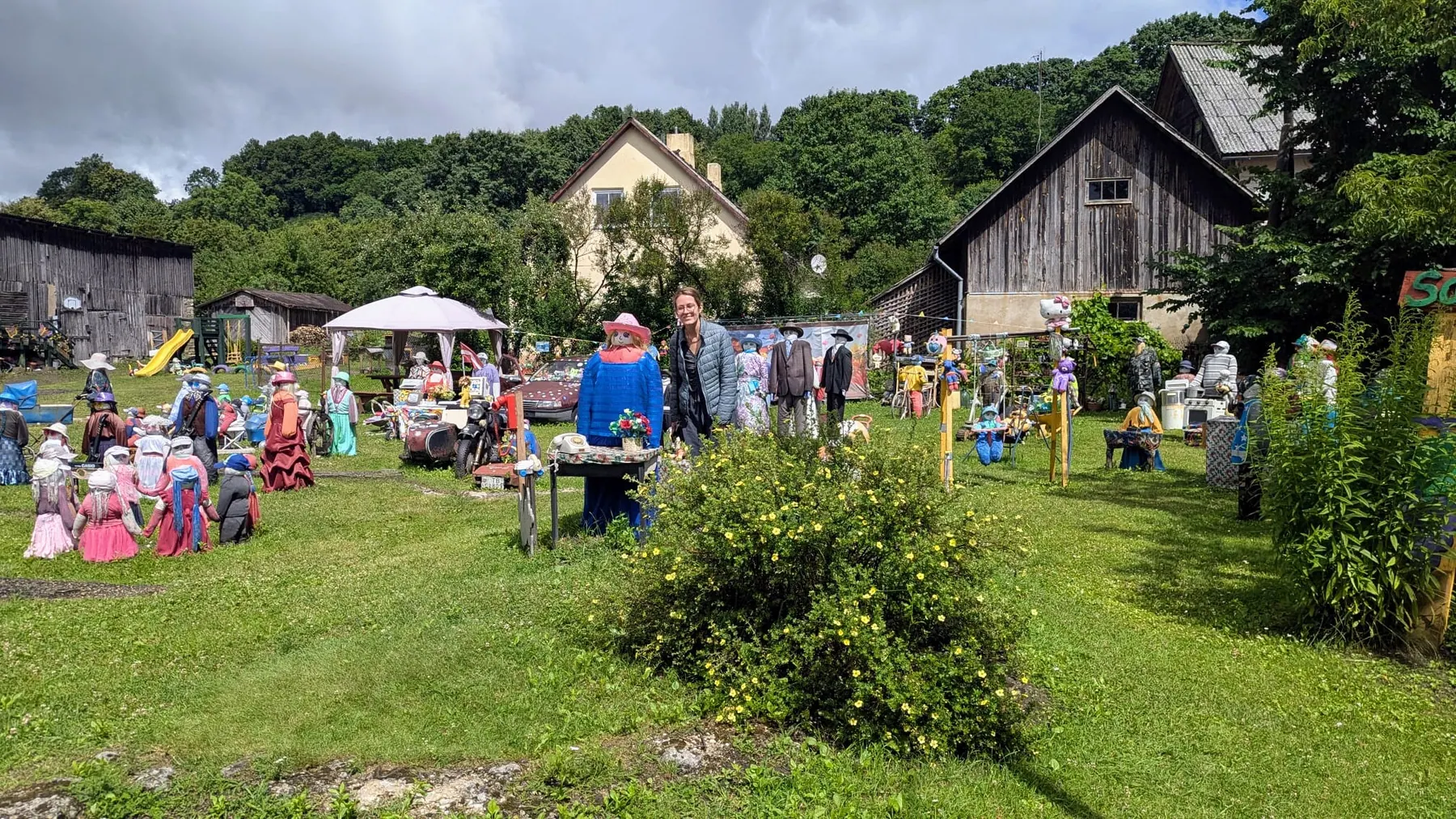 A visitor standing among the handmade figures in Sabile Doll Garden