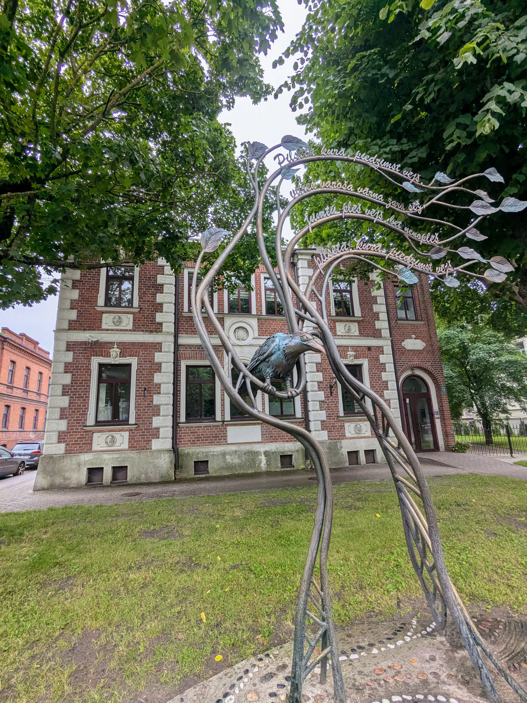 Una escultura de un personaje del himno de Liepāja entre los árboles