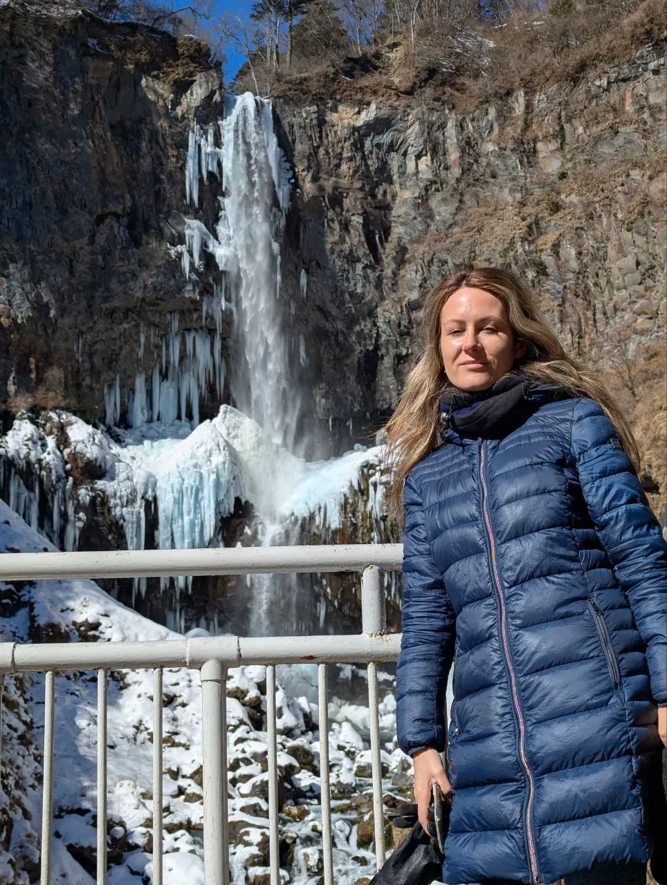 A traveller in a blue coat beside an ice-fringed waterfall in Nikko, Japan