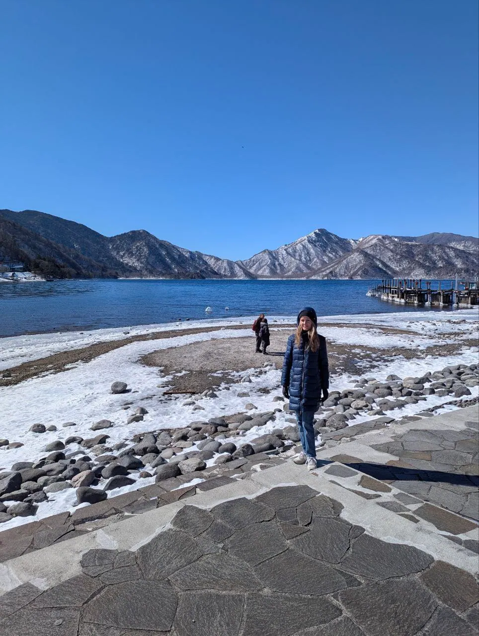 A snowy shore of Lake Chūzenji beneath the mountains