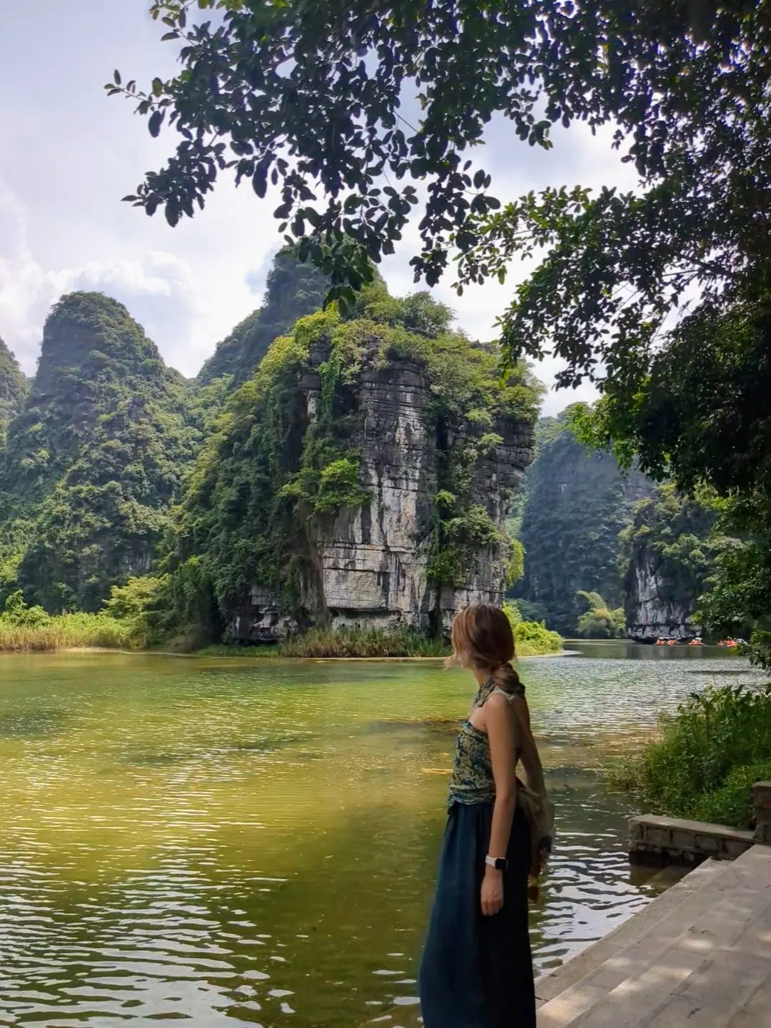 A traveller beside a calm pond beneath limestone karsts in Ninh Binh