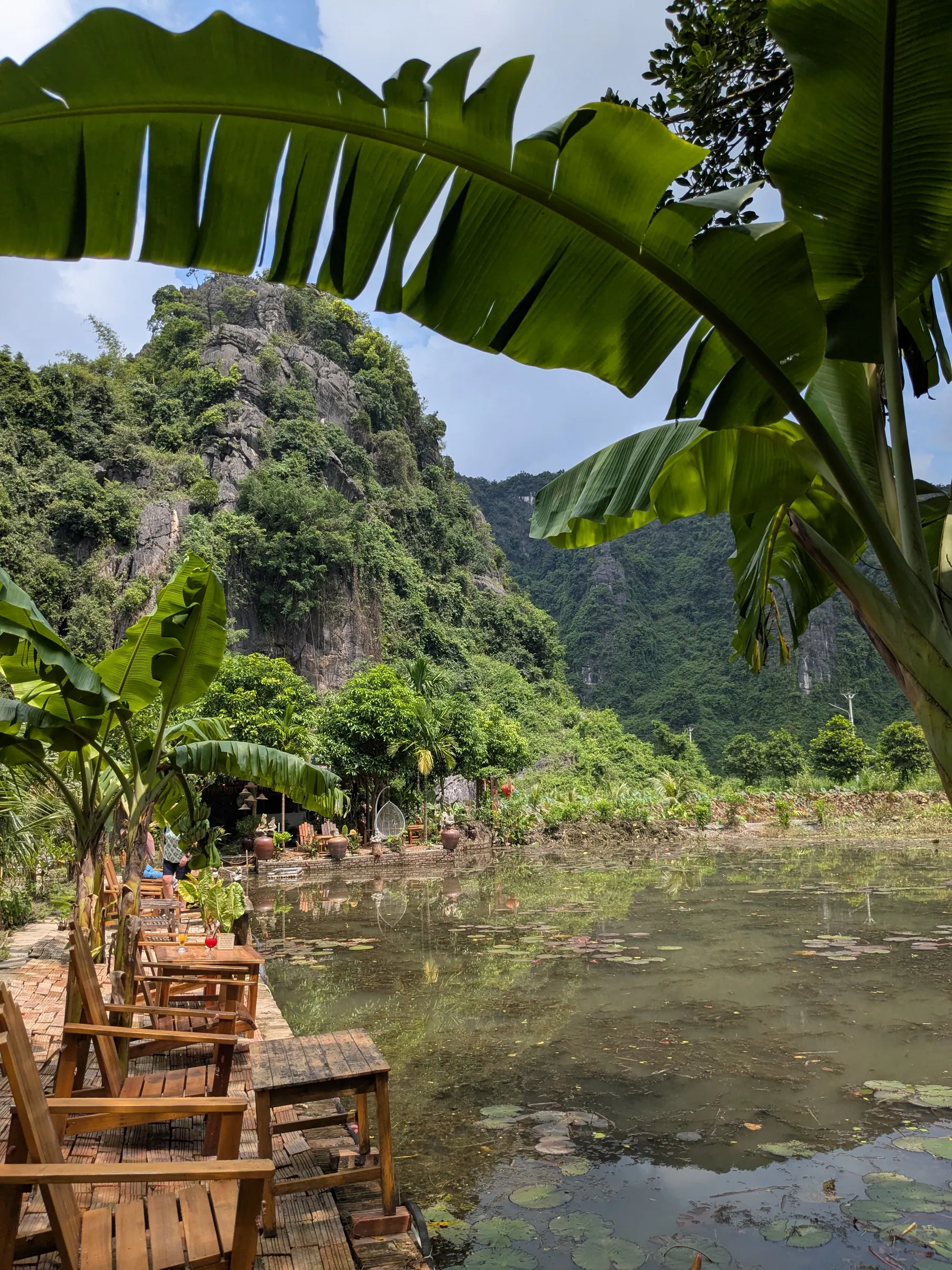A riverside cafe terrace framed by banana leaves and limestone mountains