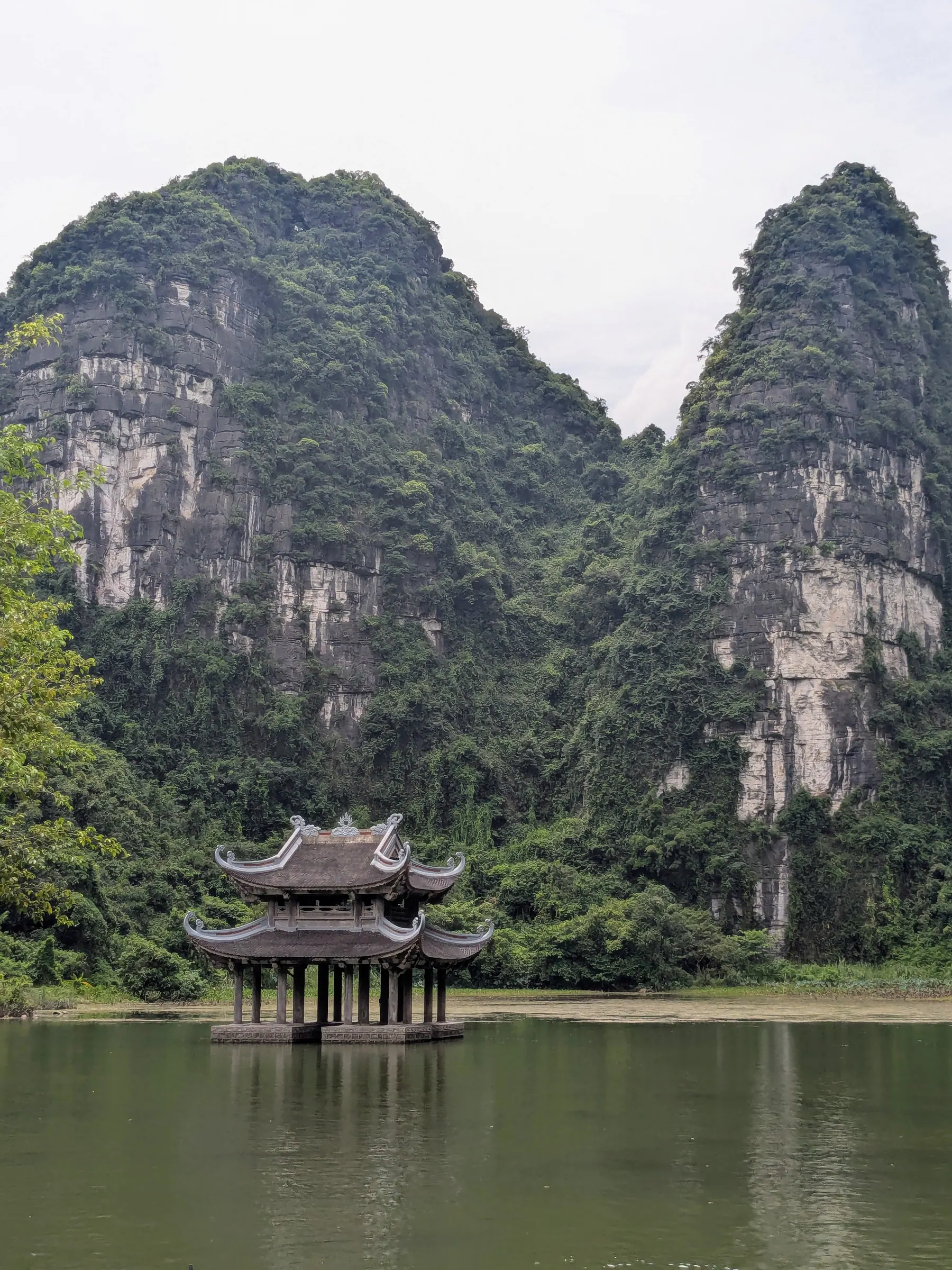 A small pagoda standing at the water's edge beneath limestone peaks