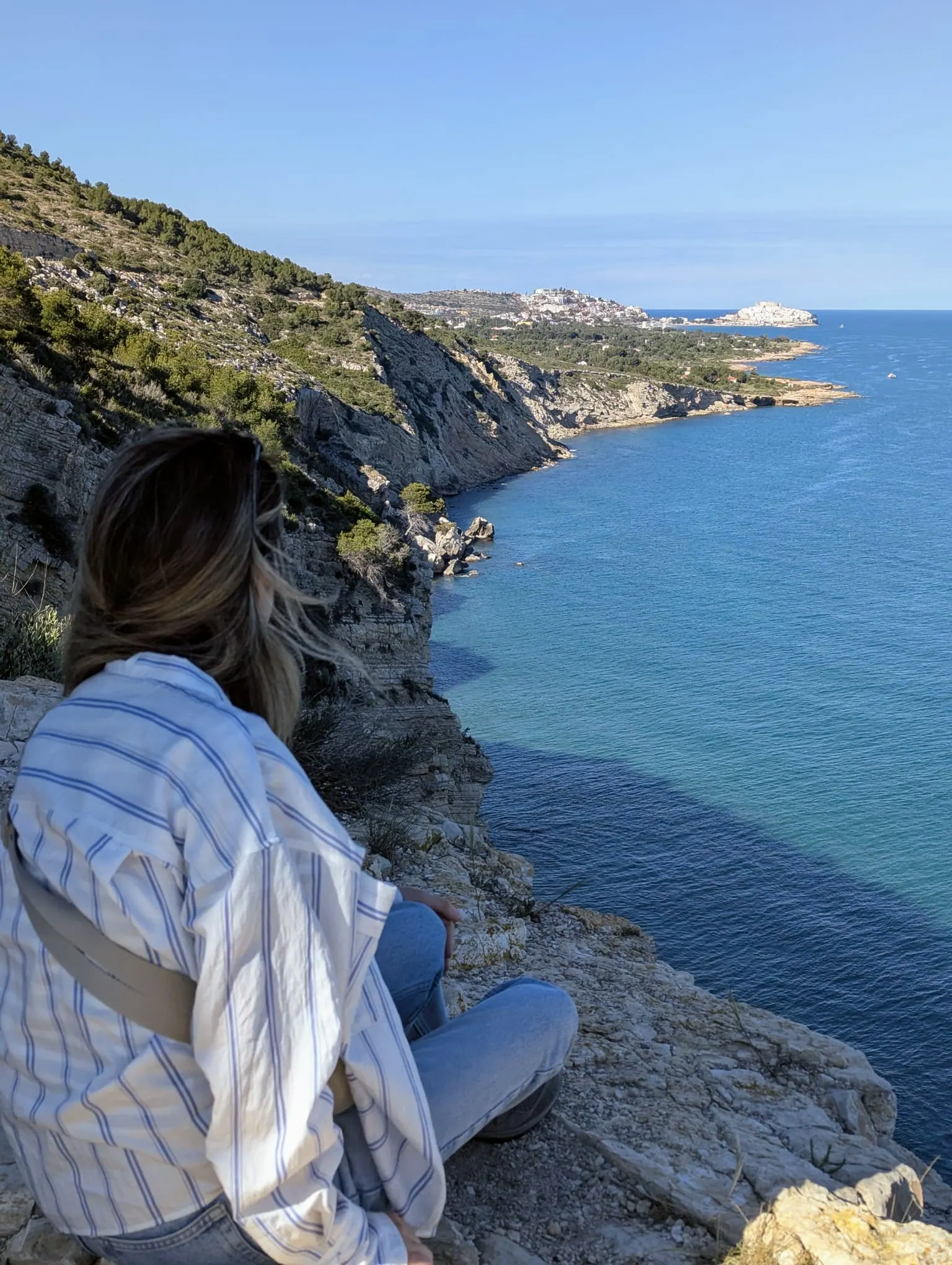 A traveler sitting above clear blue water on the rocky Sierra de Irta coast