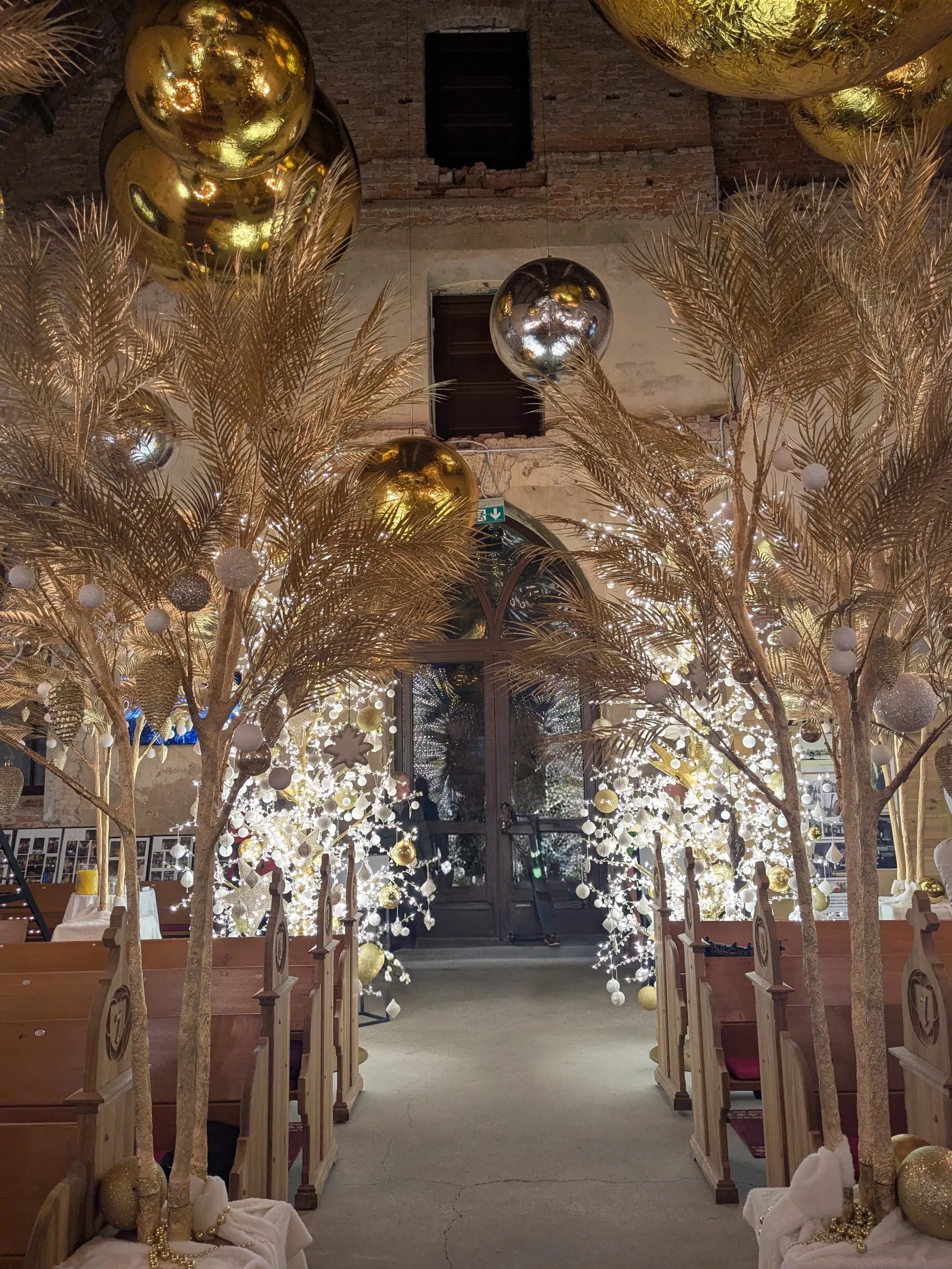 Central nave aisle of Ropaži Church framed by wooden pews, golden trees, suspended mirrored balls and fairy lights