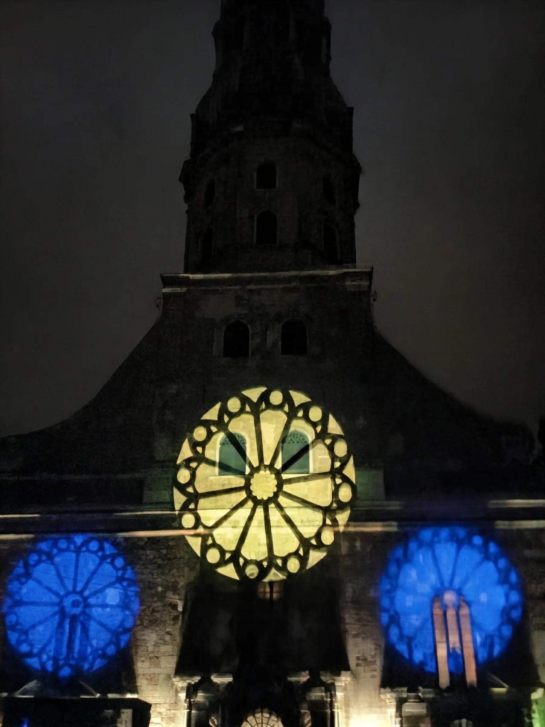 St. Peter's Church in Old Riga illuminated at night with vibrant architectural light projections across its historic facade